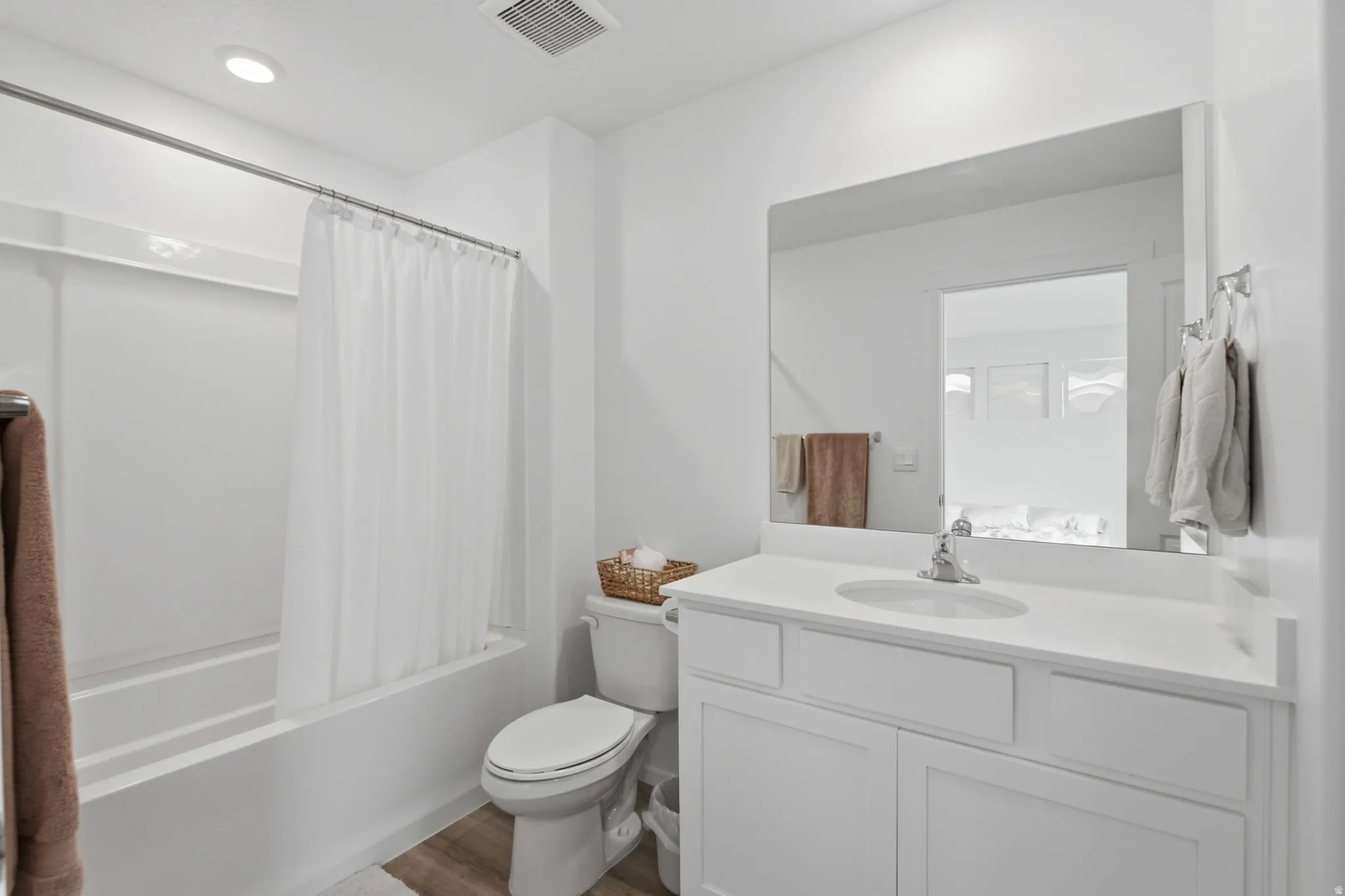 Bathroom featuring a white vanity with an undermount sink, a large wall-mounted mirror, a white toilet, and a white tub with shower