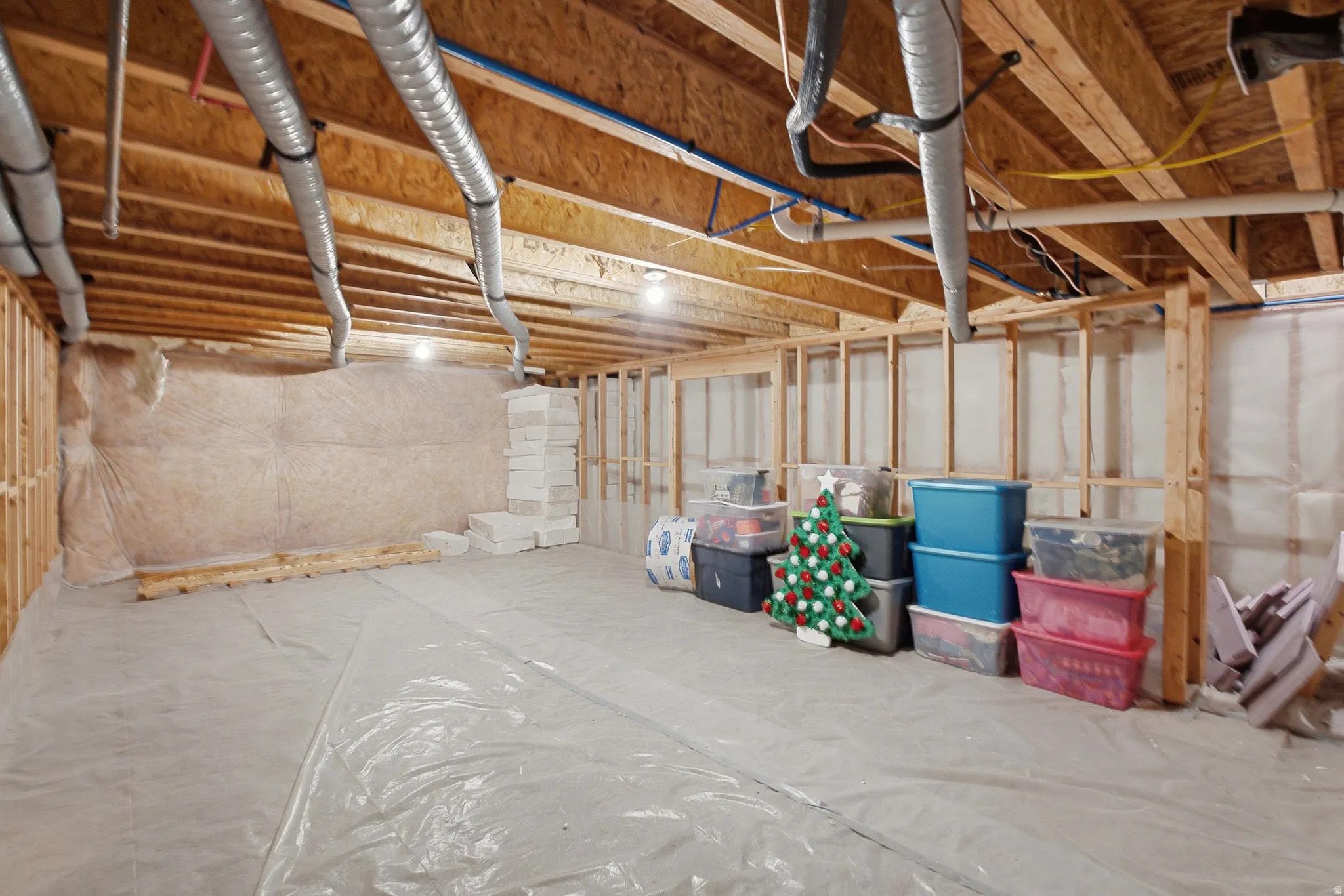 Basement featuring exposed wood joists, ductwork, and plumbing, with framed walls and insulation
