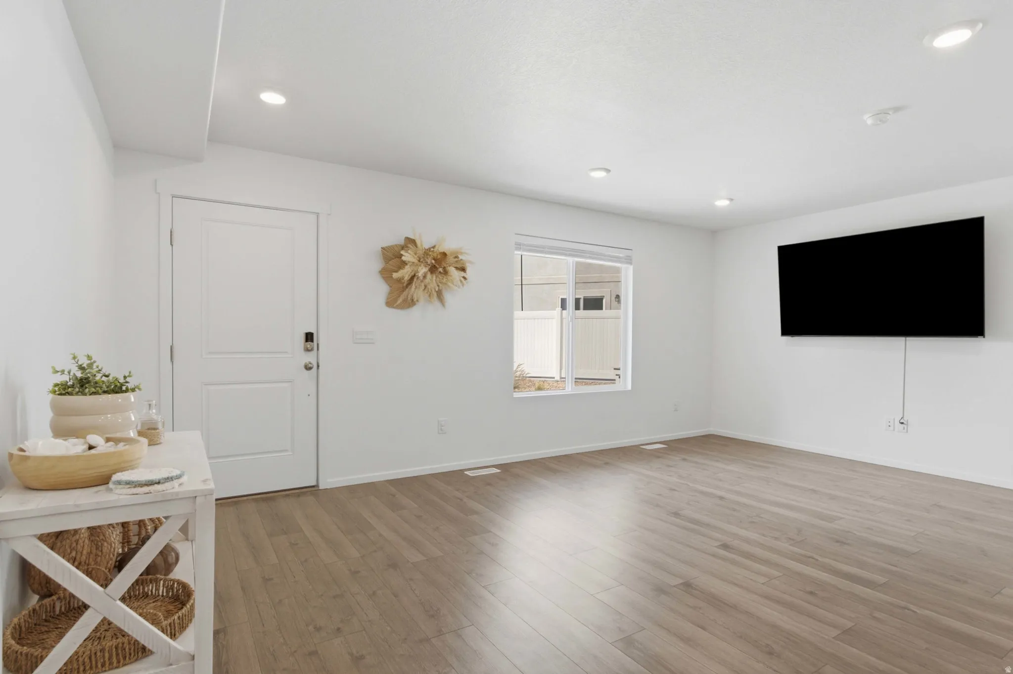 Spacious room featuring wood-finish flooring, recessed lighting, and a white paneled door