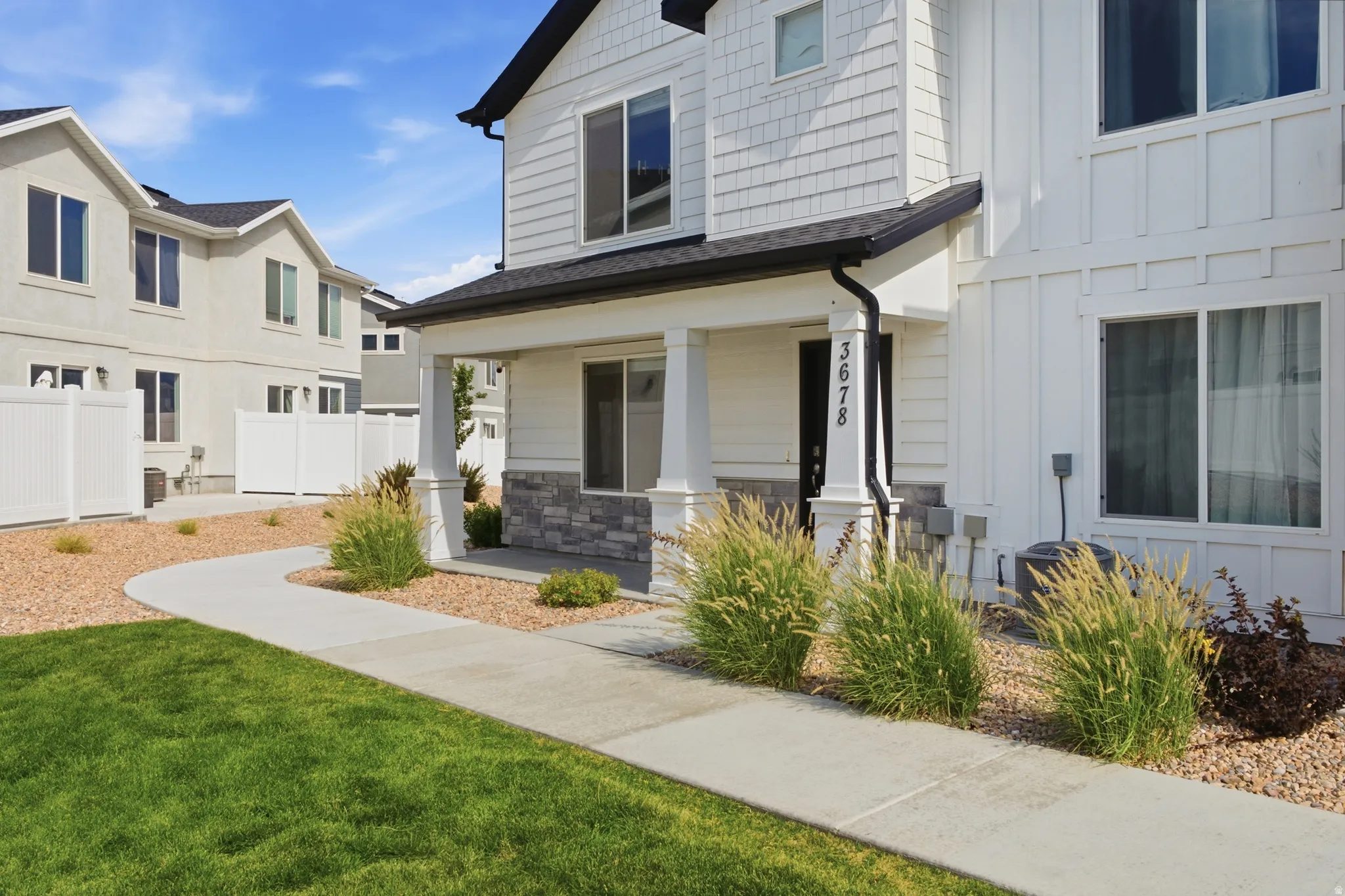 Contemporary facade featuring white siding, a covered entry with columns, and a stone accent foundation