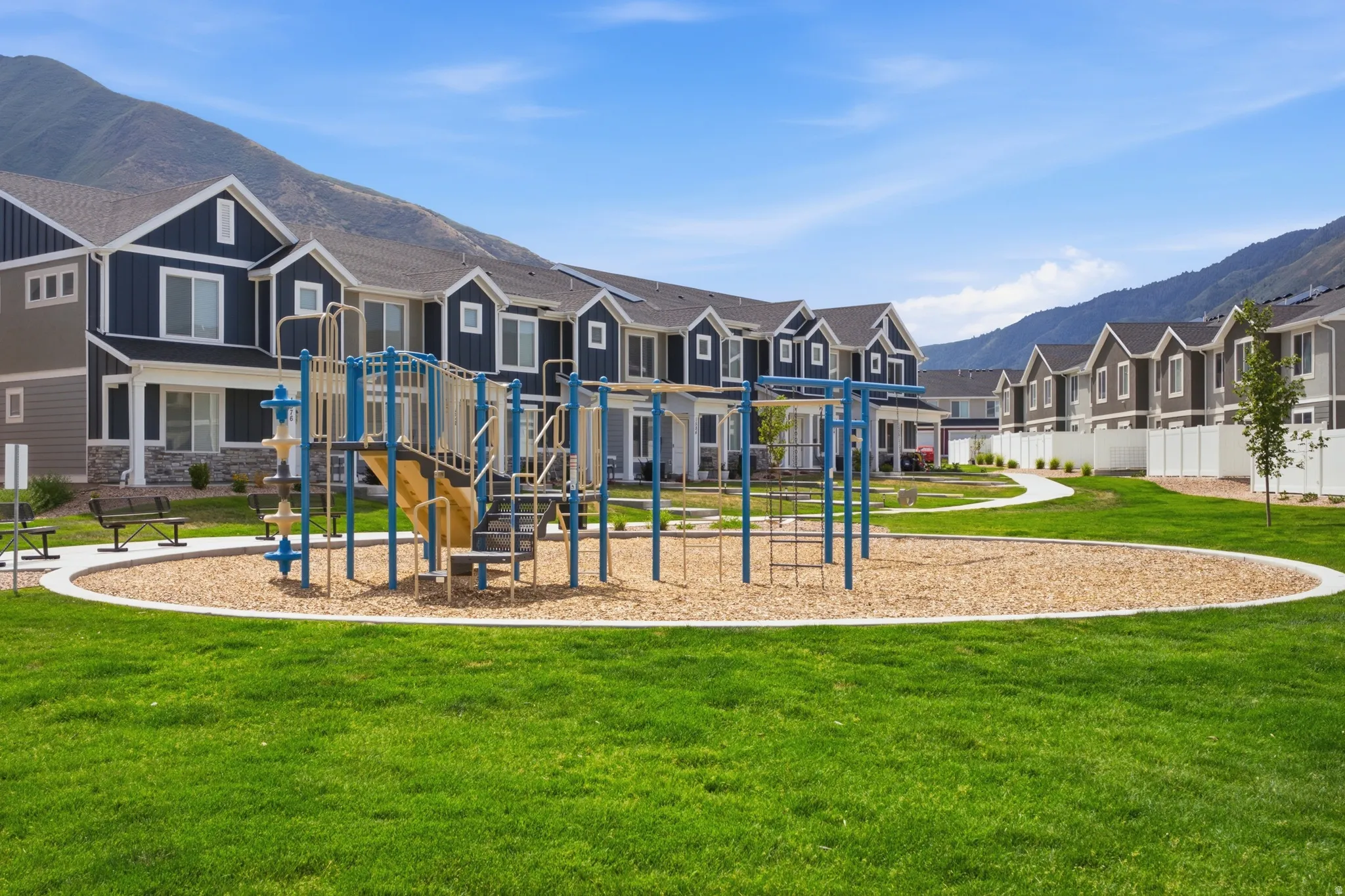 Expansive green space featuring a playground with slides and climbing structures, surrounded by a wood chip surface