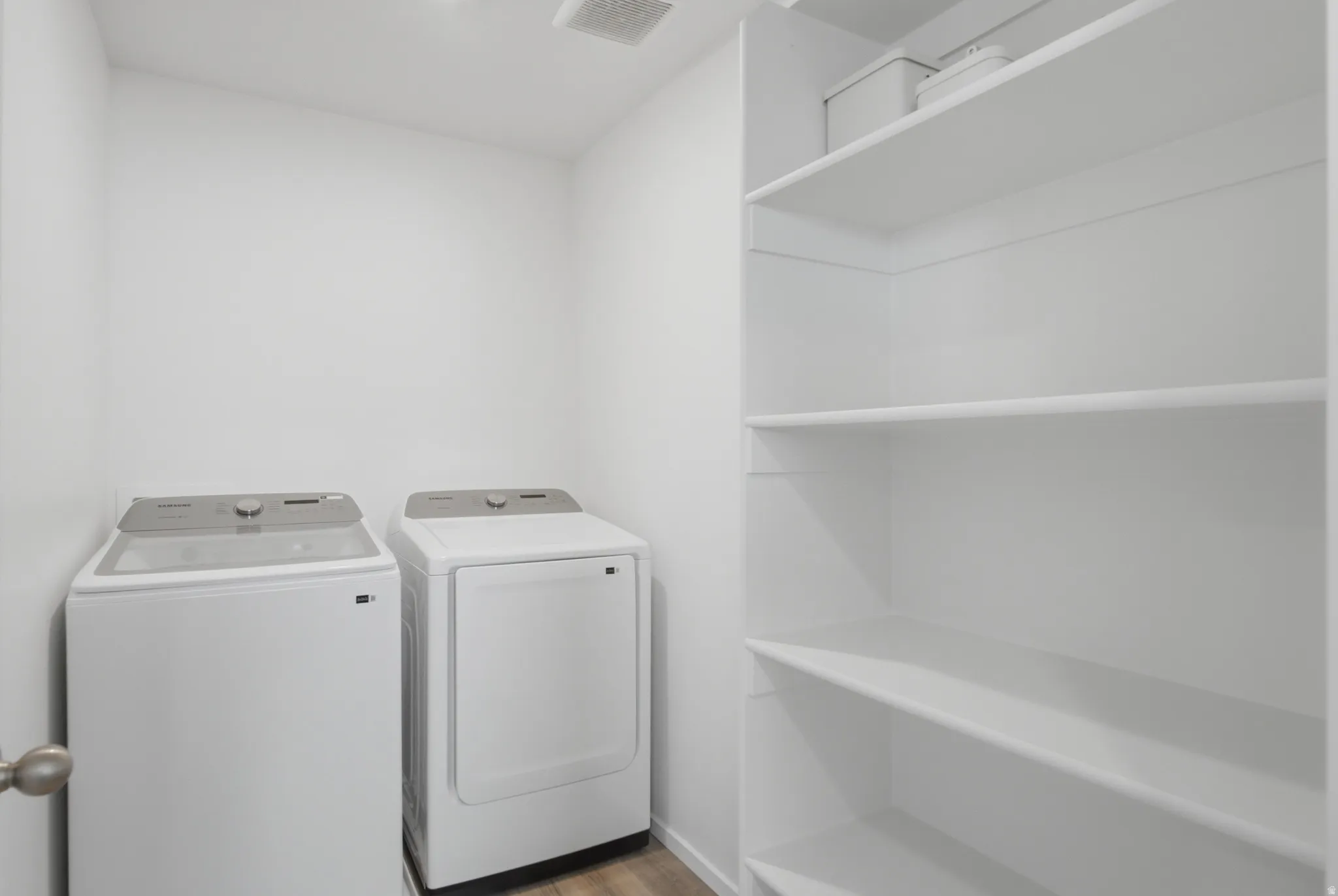 Dedicated laundry area featuring a washer and dryer, wood-finish flooring, white walls, and built-in shelving for storage