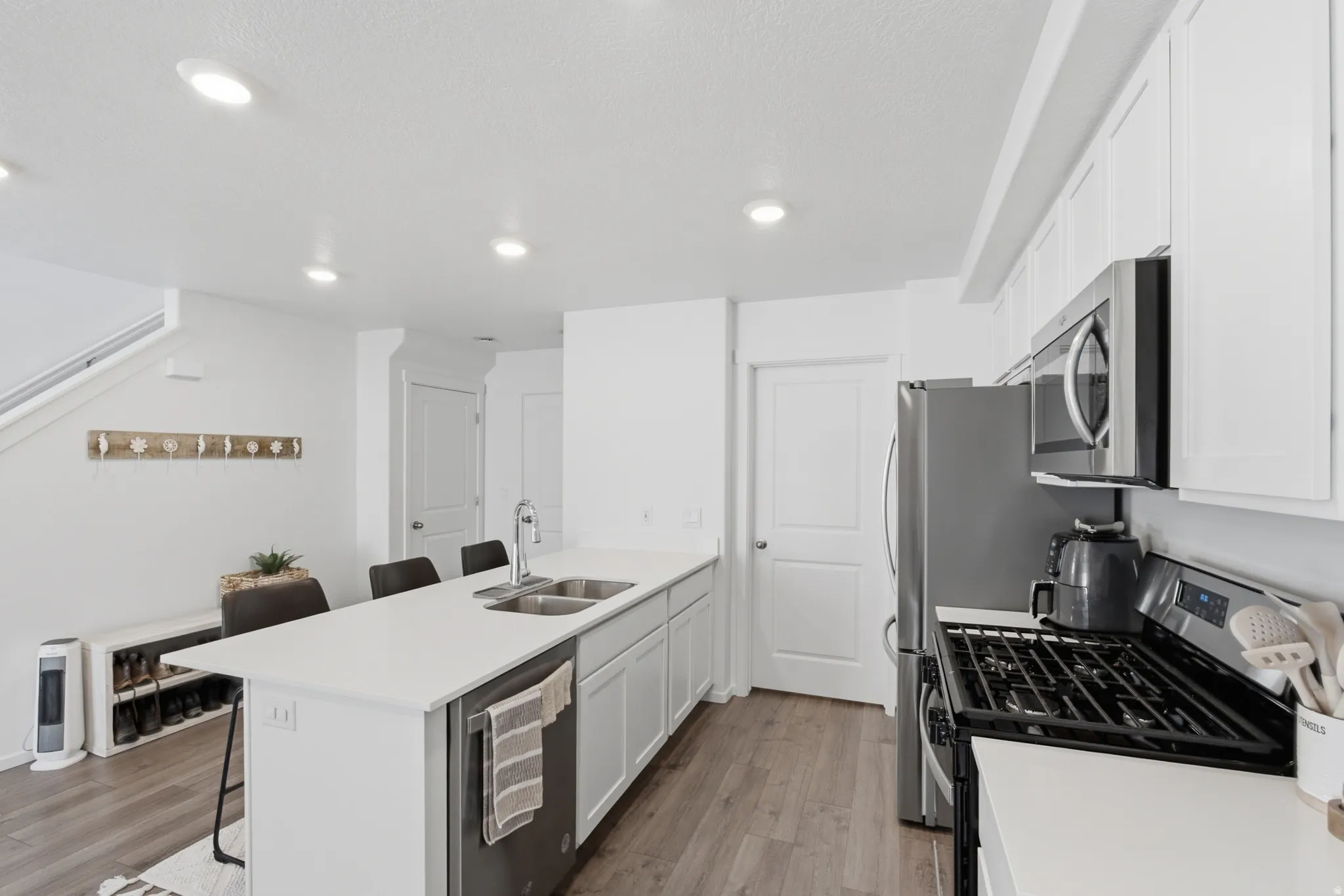 Bright kitchen featuring white cabinetry, stainless steel appliances, a white island with dual sinks, recessed lighting, and wood-finish flooring