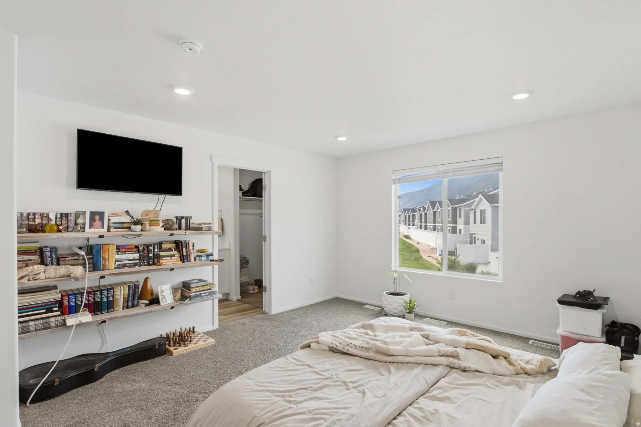 Bright bedroom with recessed lighting, plush carpet, abundant natural light, and versatile built-in shelving.