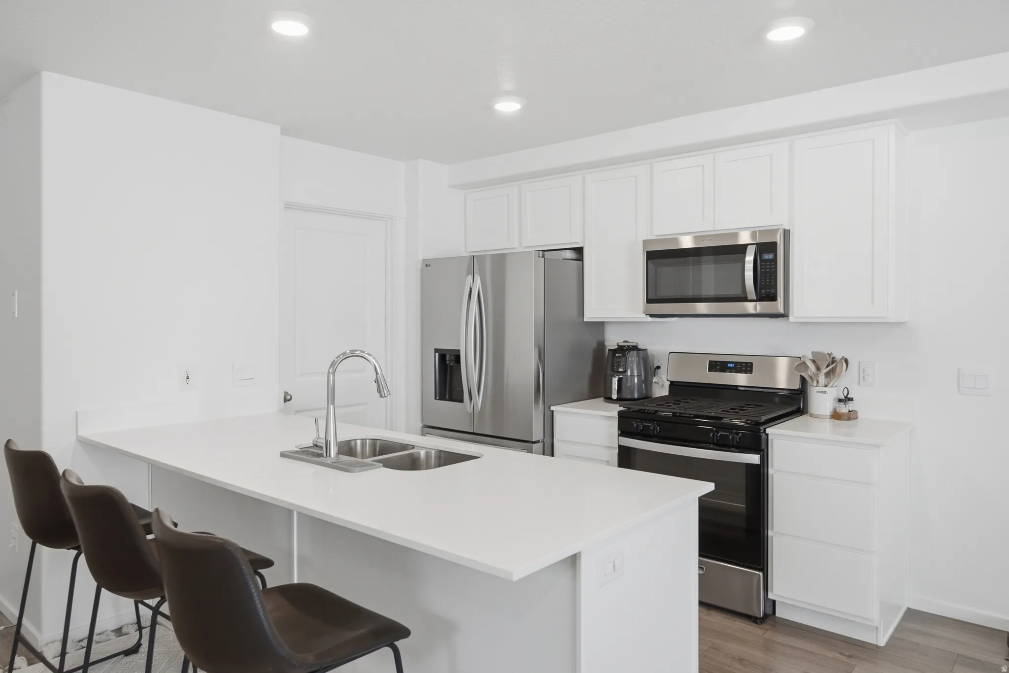 Kitchen featuring white shaker cabinetry, stainless steel appliances, recessed lighting, a dual basin sink with a high-arc faucet, and a breakfast bar with countertop seating
