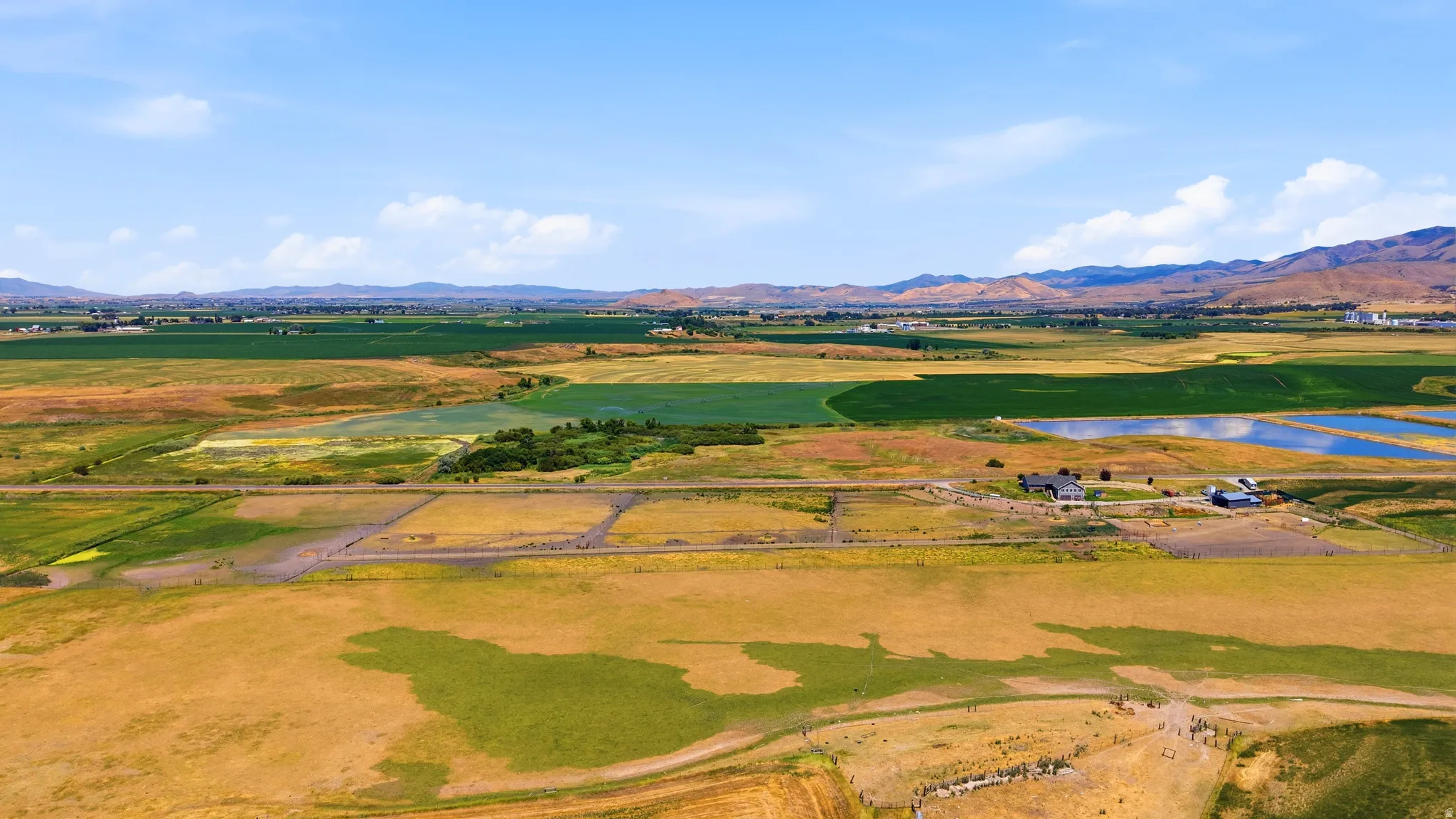 Expansive agricultural landscape featuring varied cultivated fields, scattered buildings, and distant mountain ranges