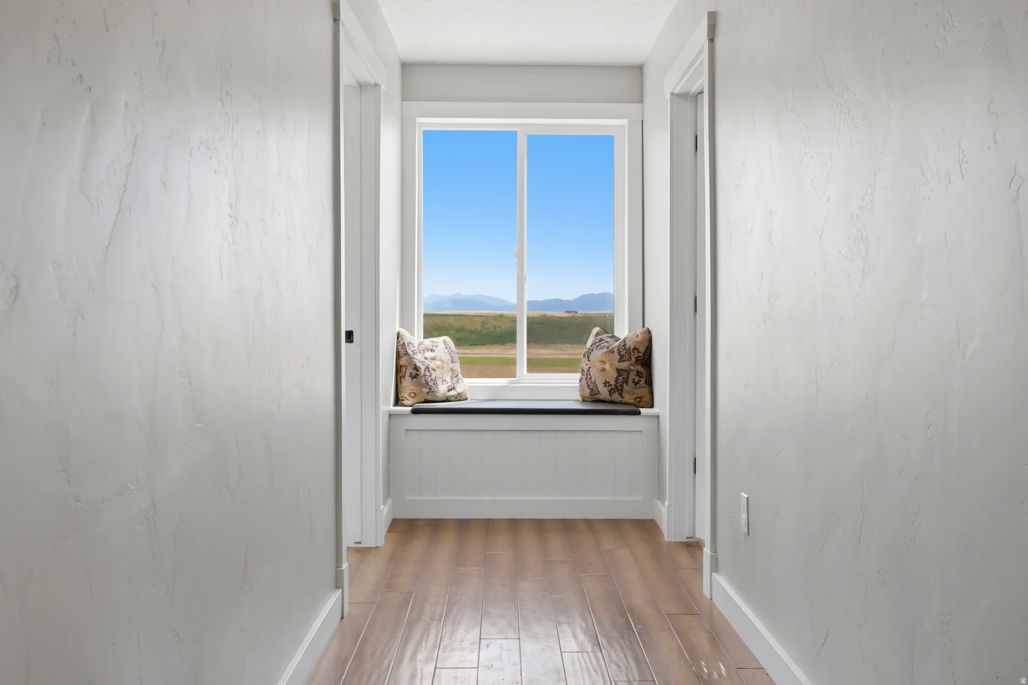 Hallway featuring wood-finish flooring, textured walls, and a built-in window seat with storage below