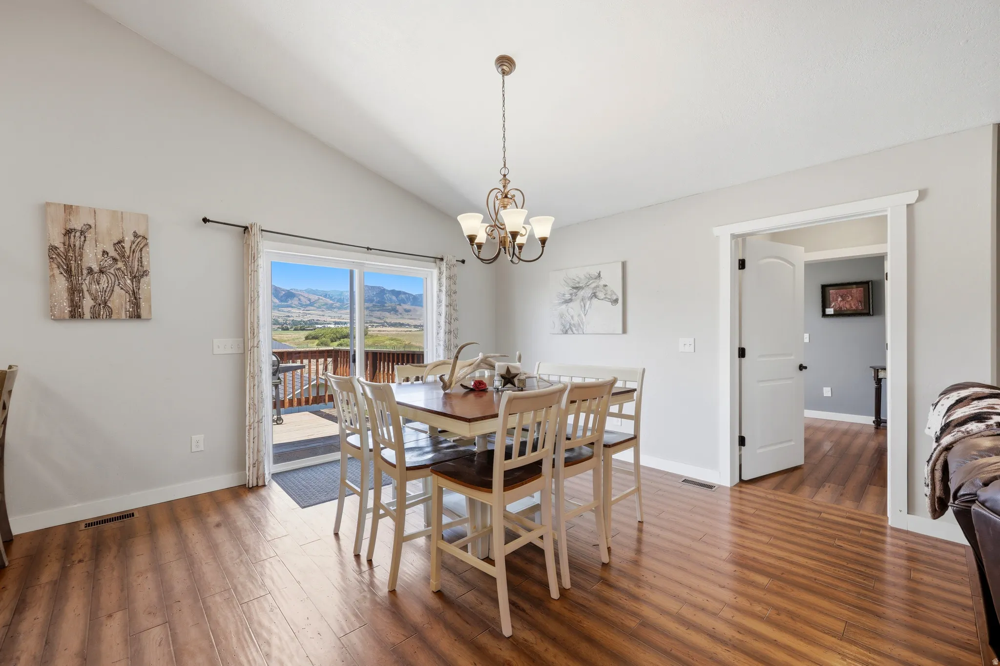 Vaulted ceiling dining area with wood-finish flooring, sliding glass door access to an exterior deck, and a classic chandelier light fixture