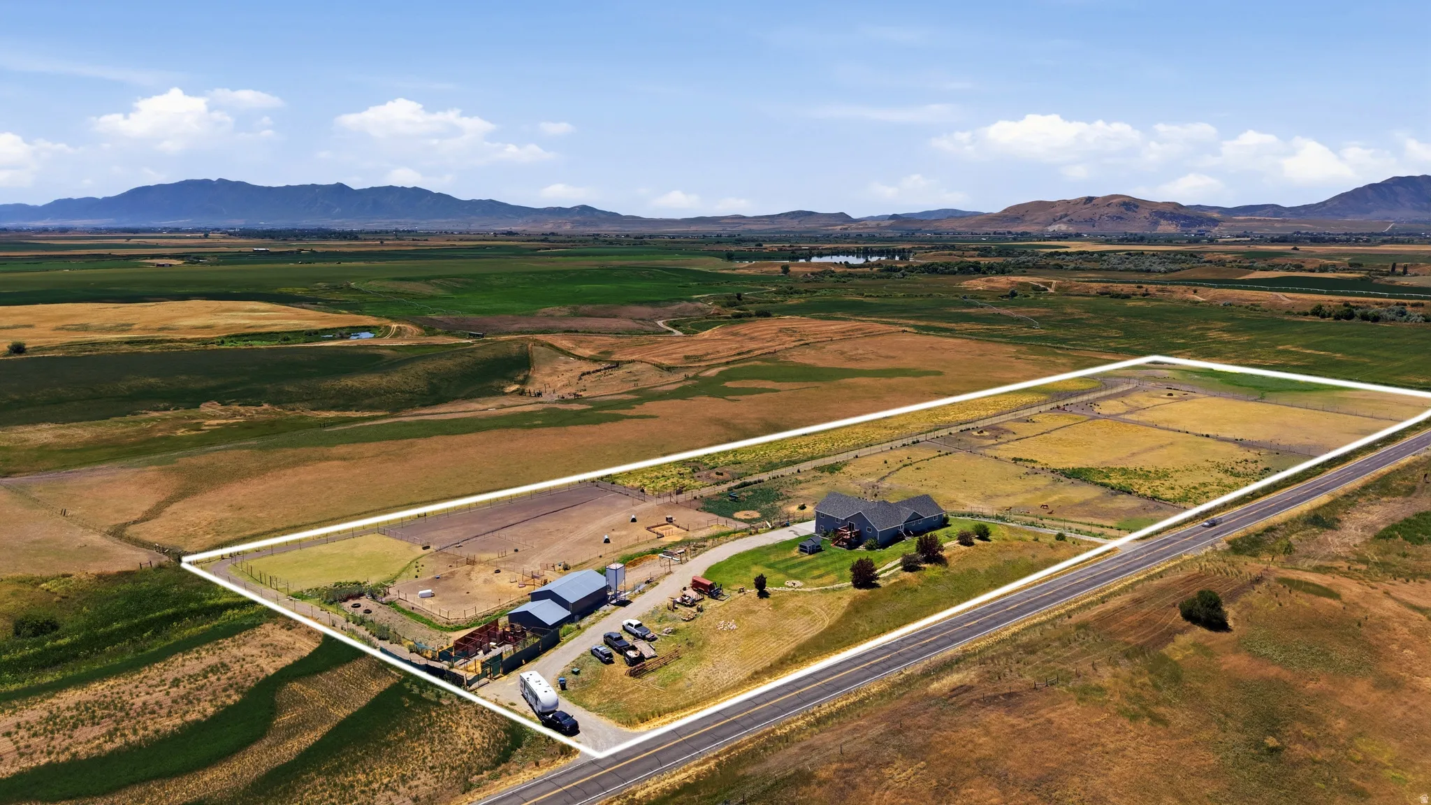 Expansive rural property featuring a dark-toned residence with a light-colored roof, multiple outbuildings, and extensive fenced areas