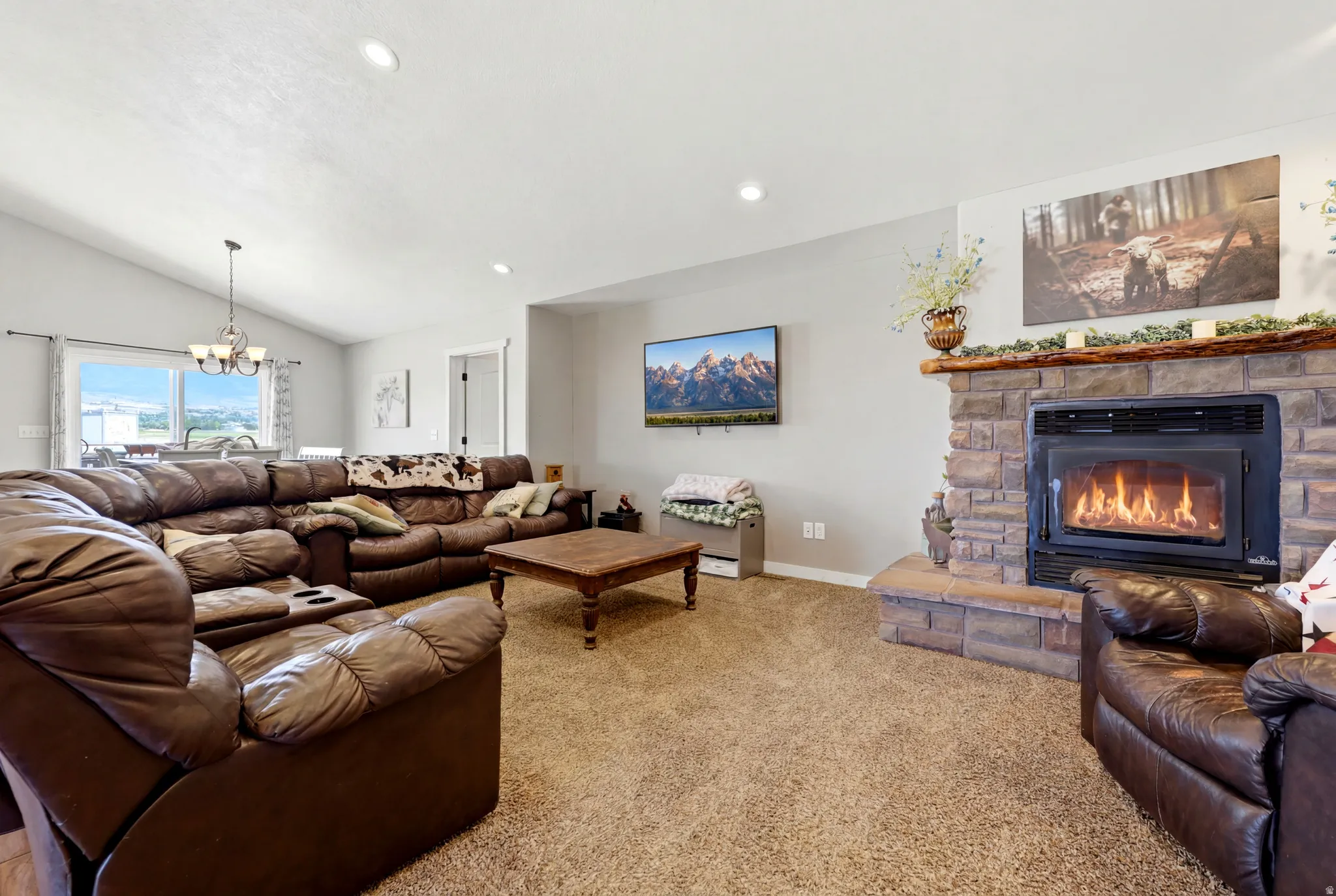 Living area featuring a stone fireplace with a wood mantle, vaulted ceilings with recessed lighting, and a window with outdoor scenery