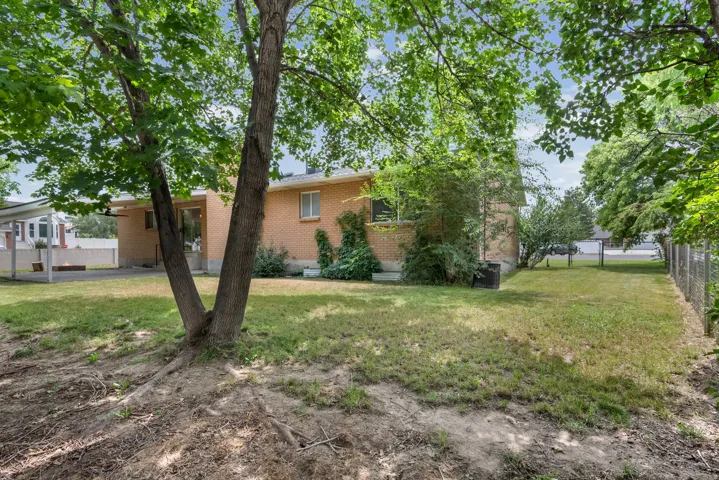 Expansive rear yard featuring mature trees, a brick exterior with white trim windows, and a covered patio area