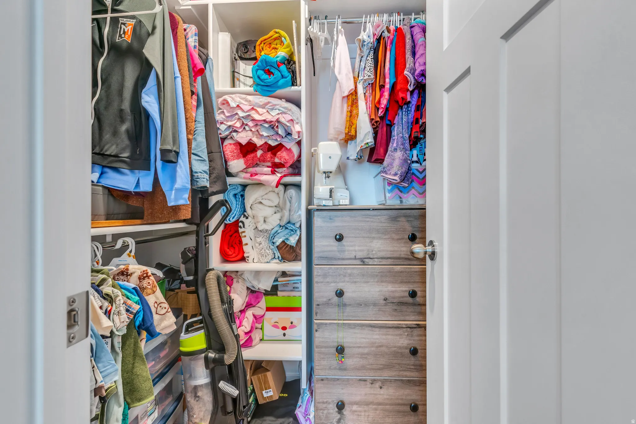 Closet with white shelving, hanging rods, and a built-in wood-finish drawer unit with dark hardware