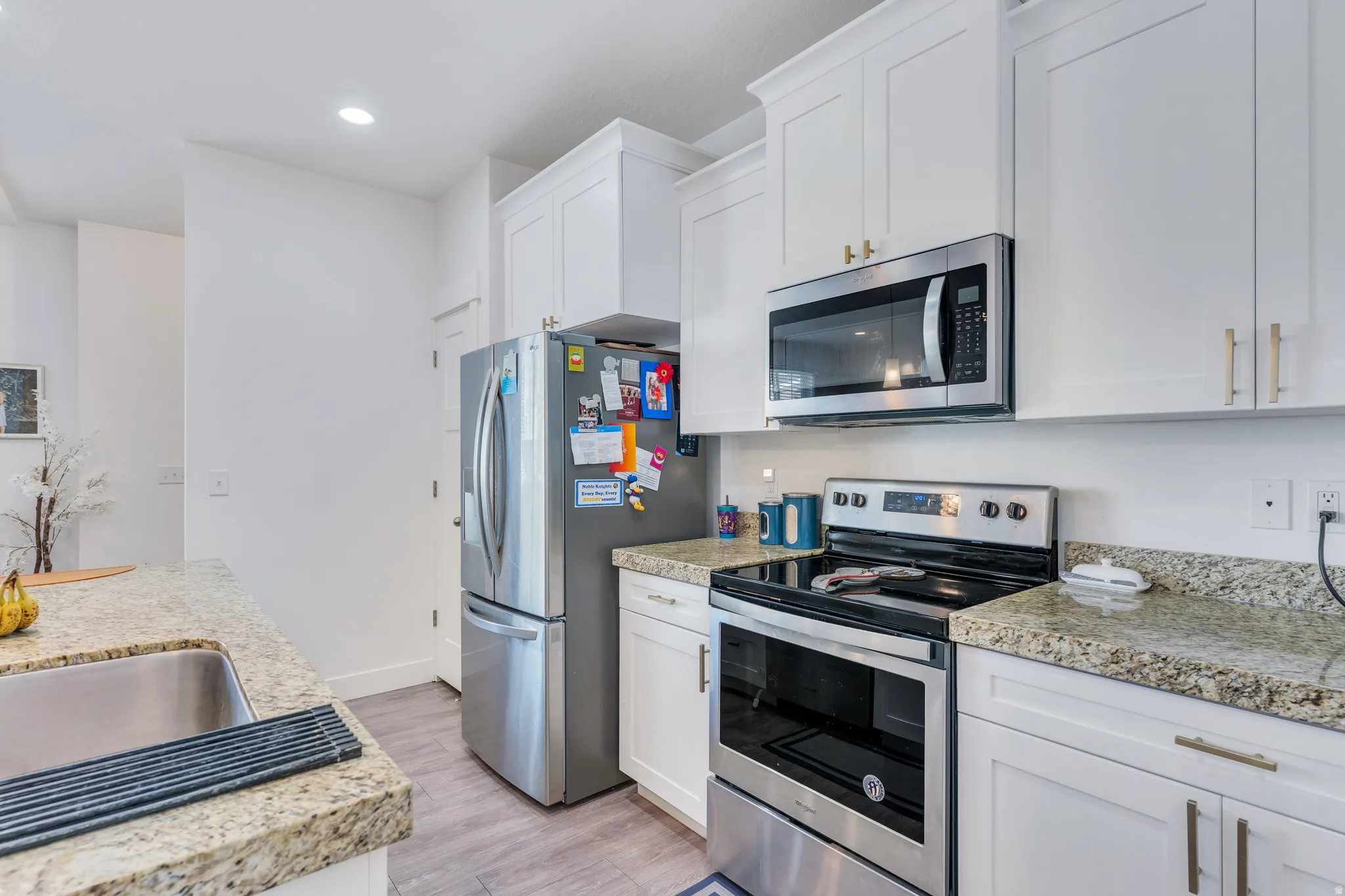 Kitchen featuring white shaker cabinetry, stainless steel appliances, speckled stone countertops, a stainless steel sink, and wood-finish flooring