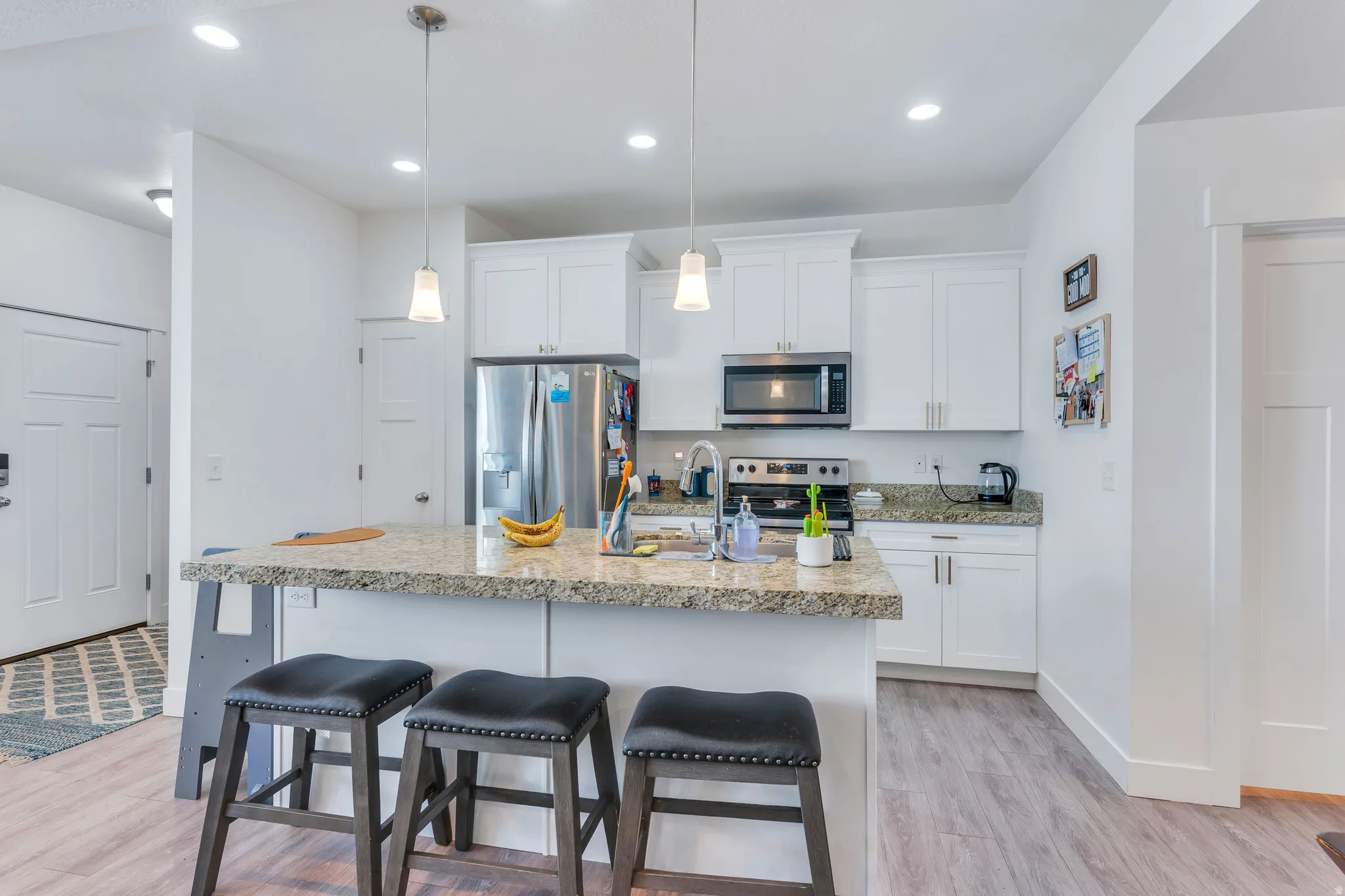 Open-concept kitchen featuring white shaker cabinetry, stainless steel appliances, granite countertops, and a kitchen island with pendant lighting