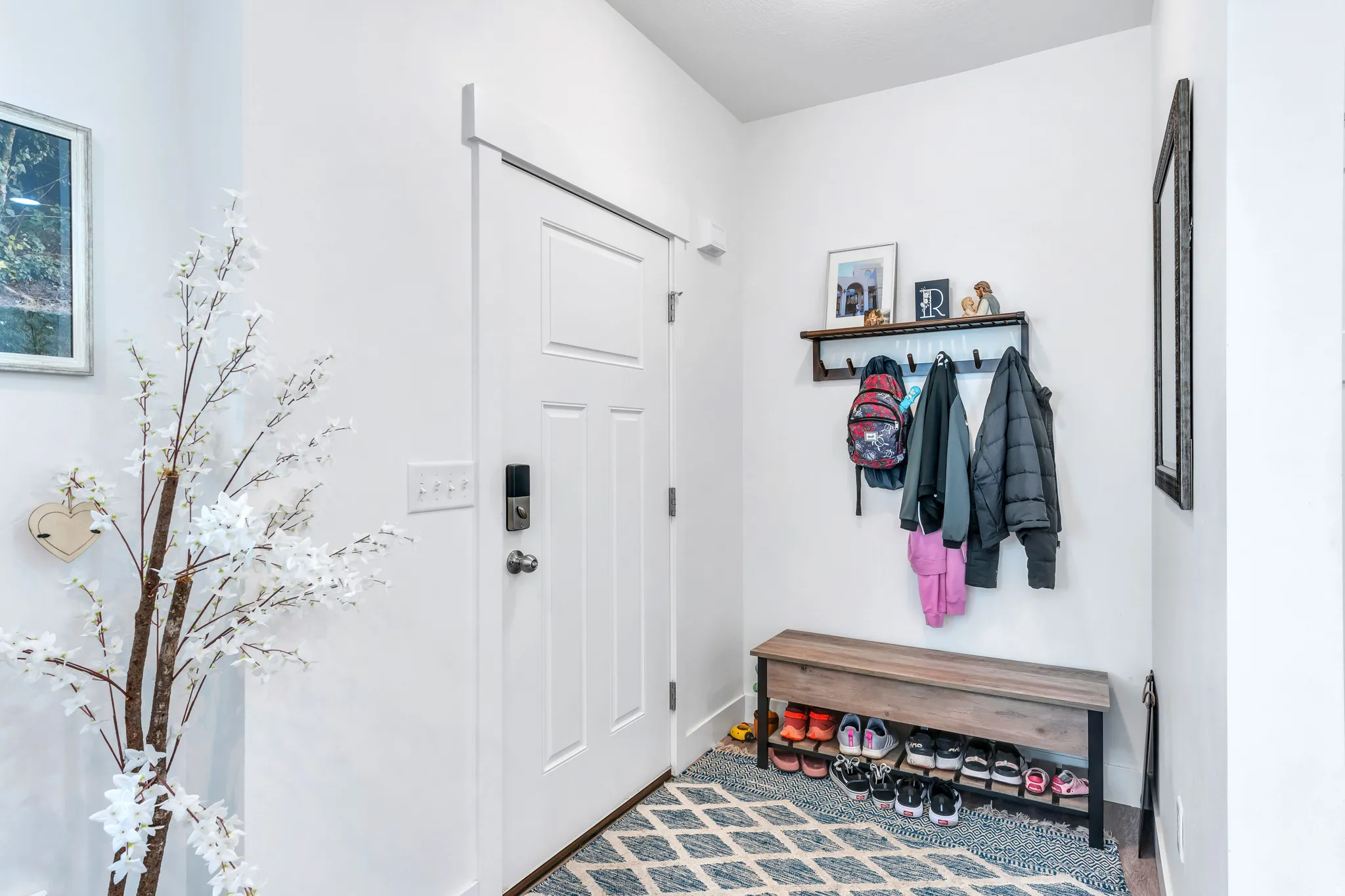 Entryway featuring a paneled door with smart lock hardware, a built-in wall shelf with coat hooks, and a wood-finish storage bench