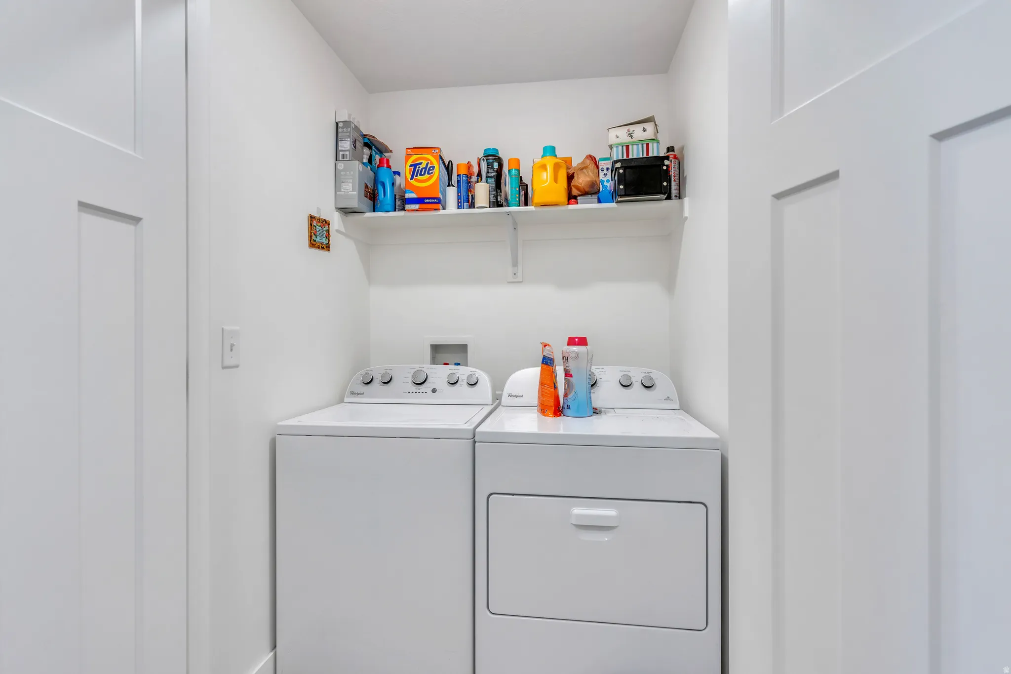 Dedicated laundry area featuring a washer and dryer set, white wall shelving, and a clean white color palette