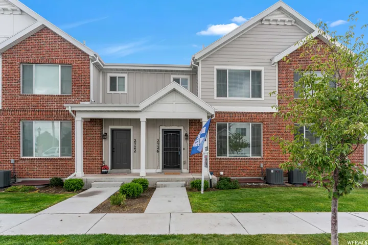 Townhome exterior featuring brick and siding accents, white trim, a covered porch, and a manicured lawn