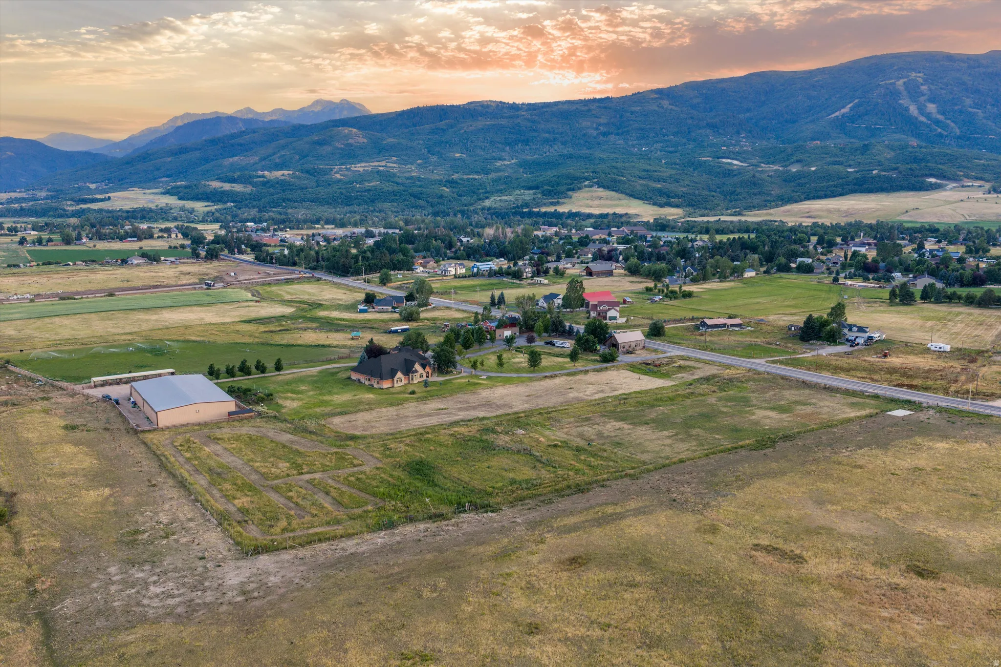 Expansive rural landscape featuring a prominent large outbuilding, extensive undeveloped land, a paved road, and distant mountain ranges