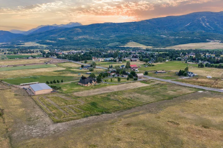 Expansive rural landscape featuring a prominent large outbuilding, extensive undeveloped land, a paved road, and distant mountain ranges