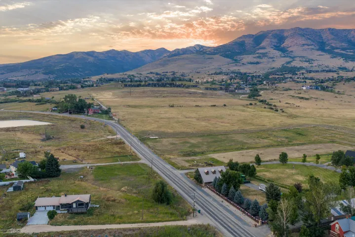 Expansive mountain landscape with a meandering roadway, scattered residential properties, and a prominent pond