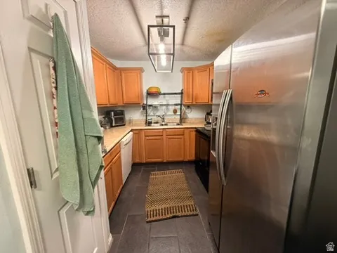 Kitchen featuring stainless steel refrigerator, L-shaped laminate countertops, wood cabinetry, and dark tile flooring