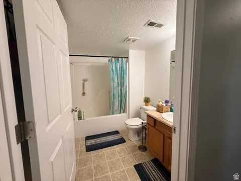 Bathroom featuring a tub and shower combination with a gold-finish shower head, a toilet, a wood-finish vanity with a single sink, and square tile flooring