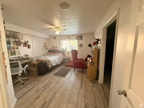 Spacious room featuring wood-finish flooring, a ceiling fan with integrated lighting, a large window, and white walls