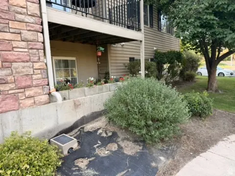 Stone and siding exterior with a ground-level window, concrete retaining wall, and established landscaping