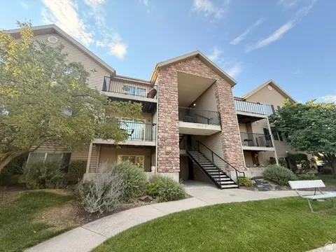 Multi-story residential building featuring a stone and siding exterior, multiple balconies with black railings, and a prominent exterior staircase