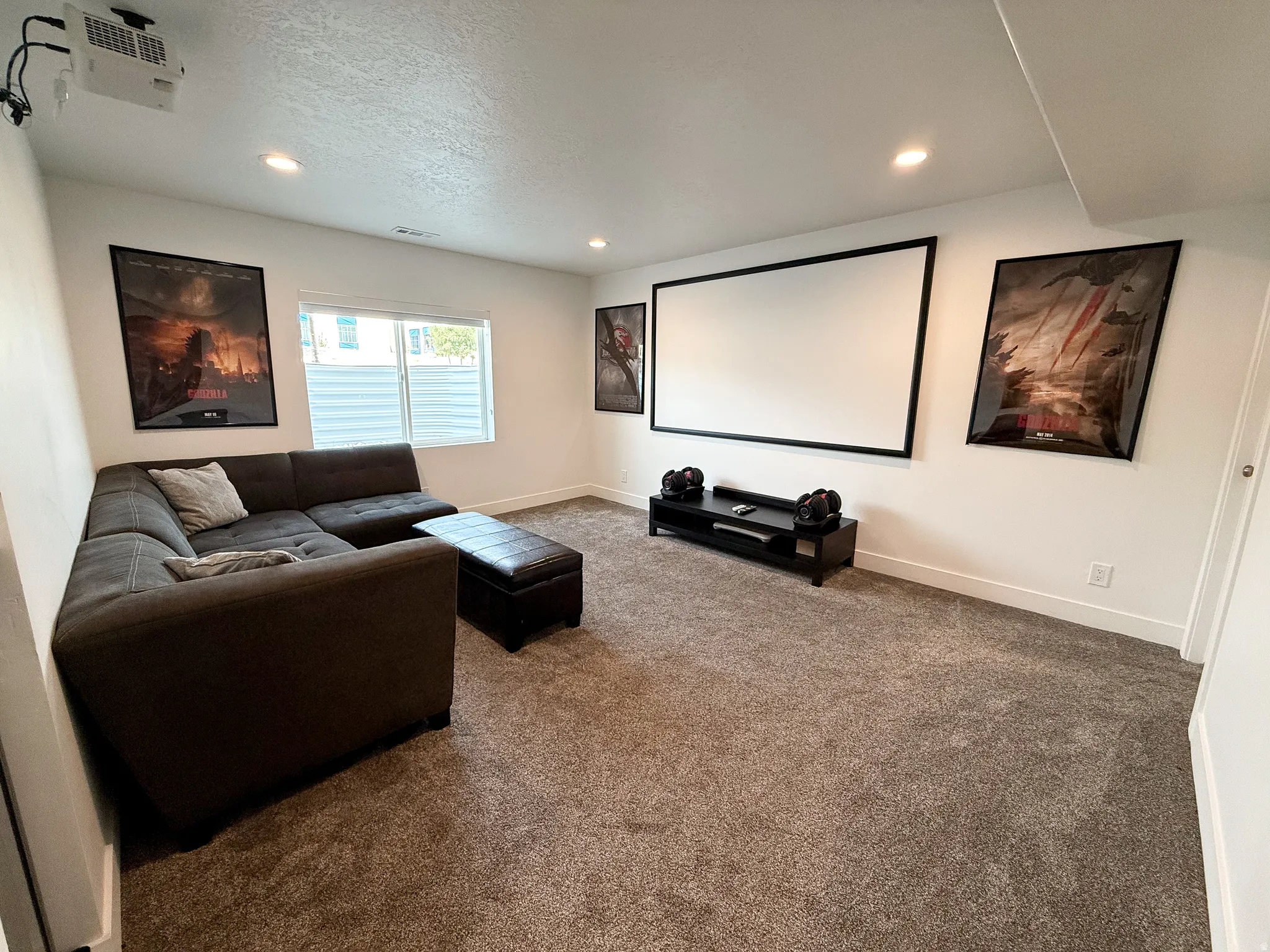 Spacious media room featuring a large projection screen, recessed lighting, and soft gray carpet flooring
