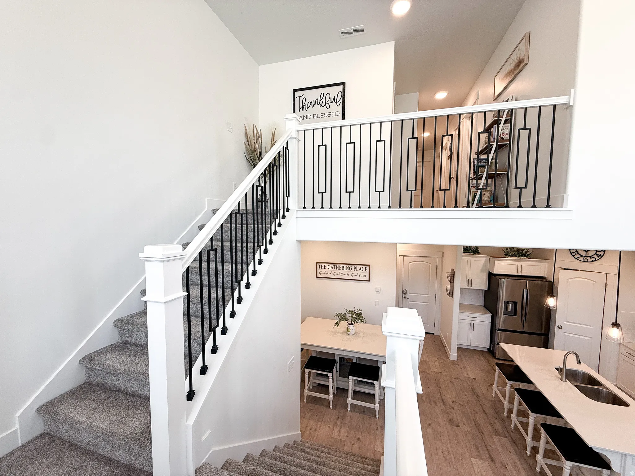 Two-story interior featuring a carpeted staircase with white newel posts and black wrought iron balusters