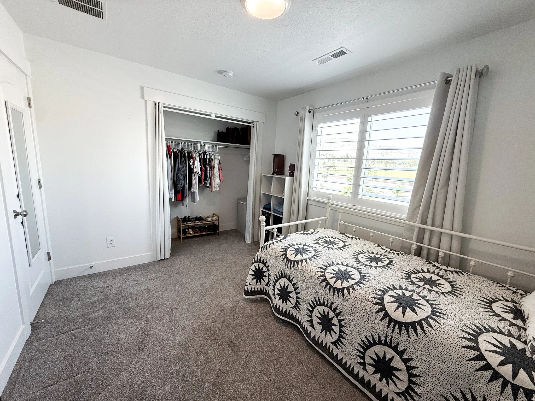 Bright room featuring a window with plantation shutters, a spacious closet with double doors, and soft gray carpeting