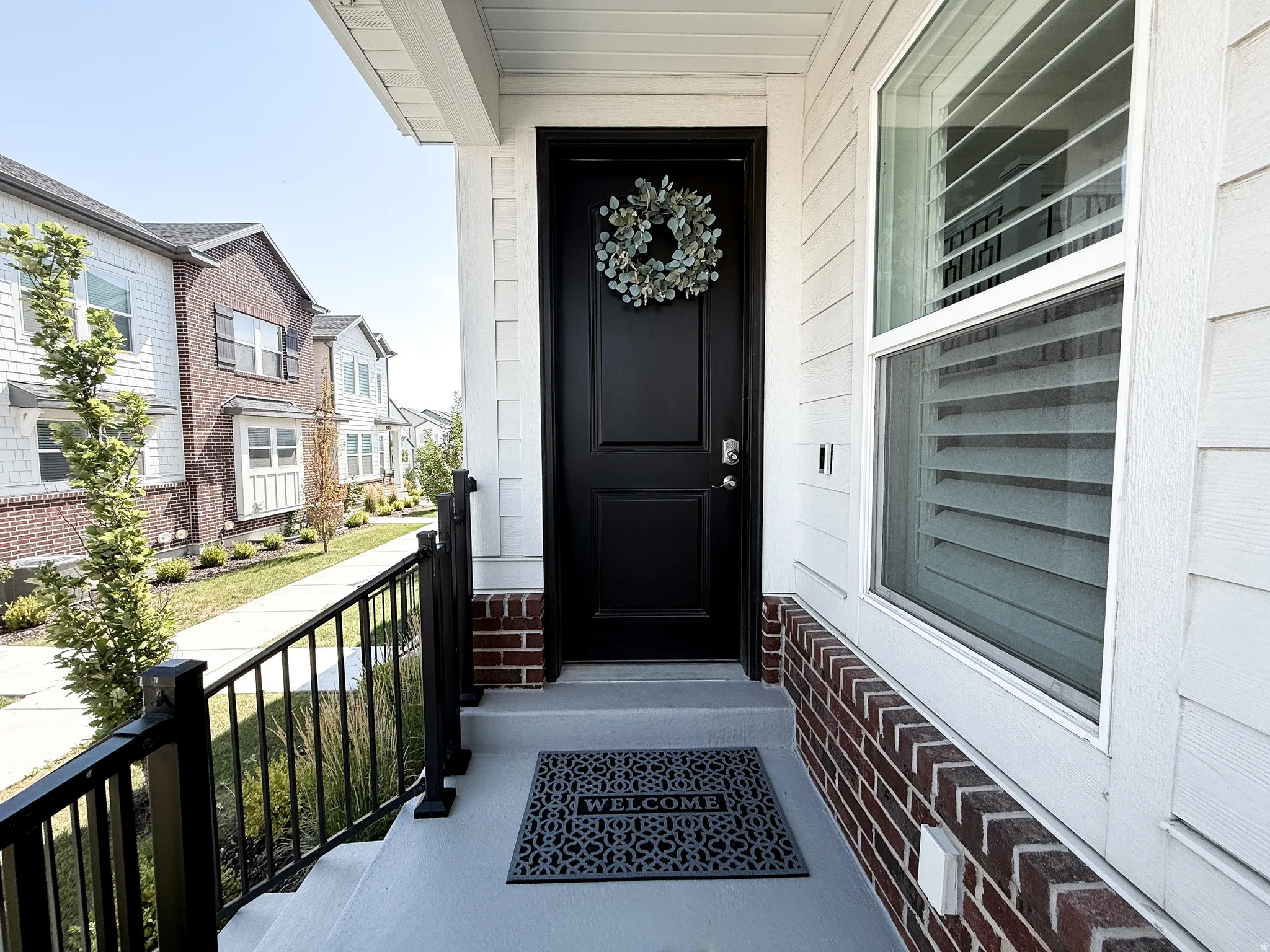 Entryway featuring a black panel door, white siding, brick accents, and a window with interior blinds