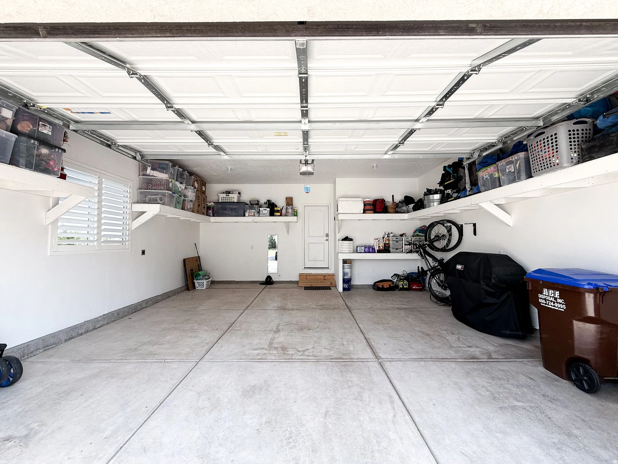 Spacious garage featuring a finished concrete floor, white walls, and built-in overhead shelving