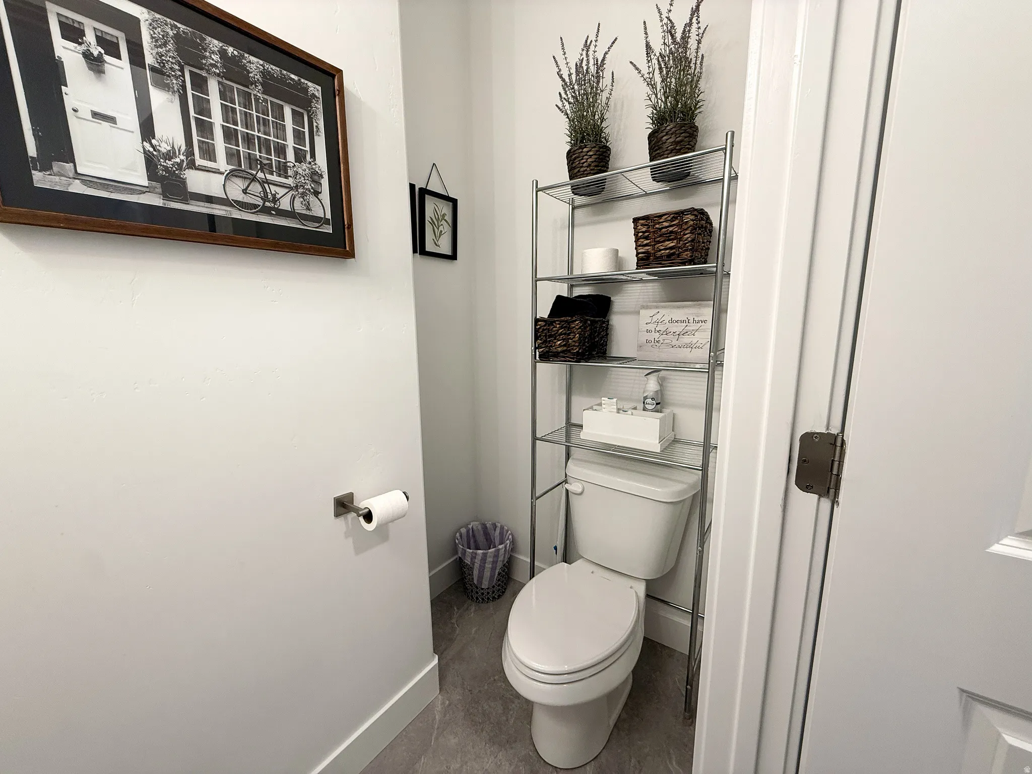 Compact water closet featuring a white commode, gray tile flooring, and white baseboards
