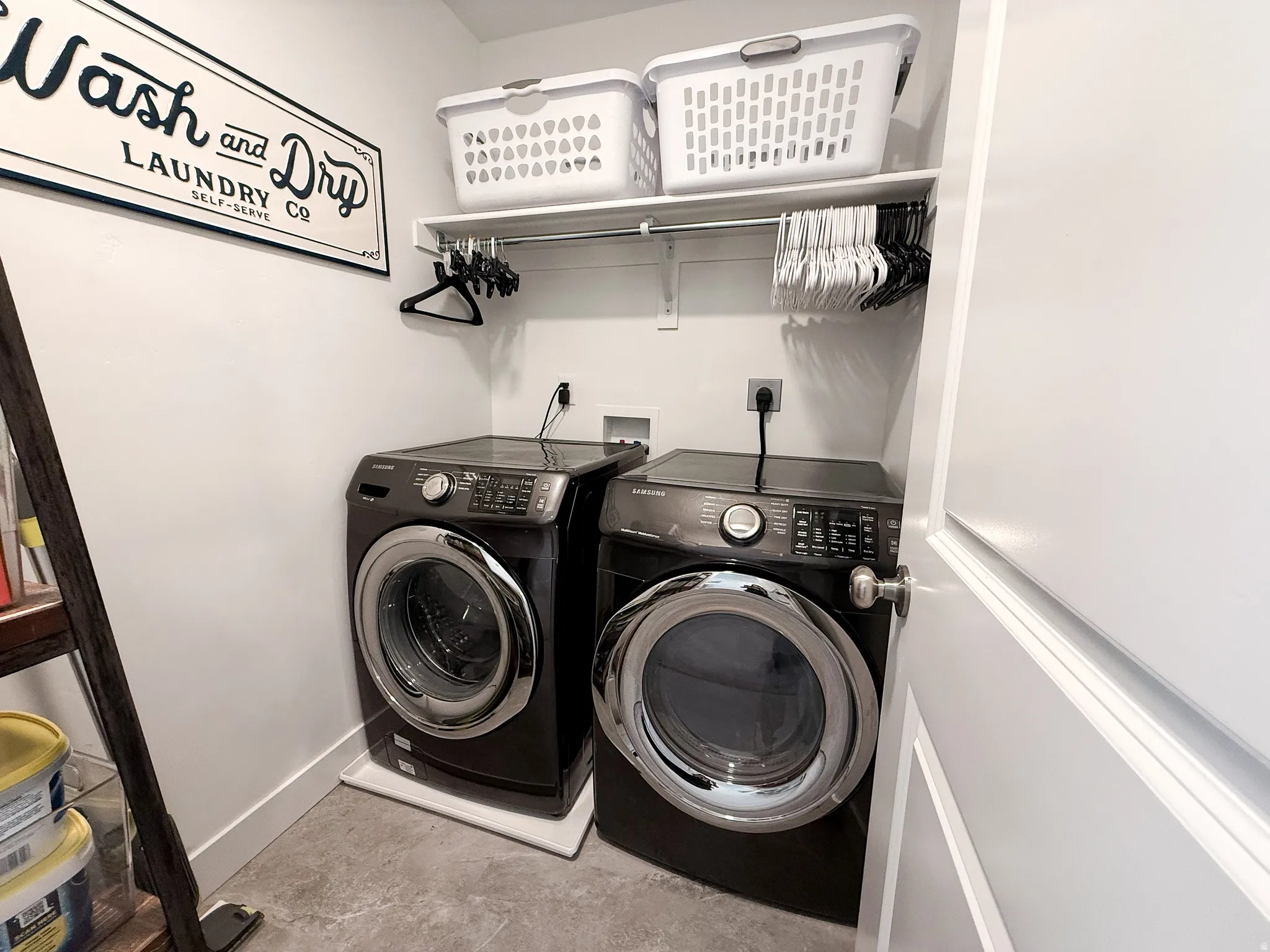 Dedicated laundry area featuring a front-load washer and dryer, concrete-finish flooring, and a built-in storage shelf with hanging rod