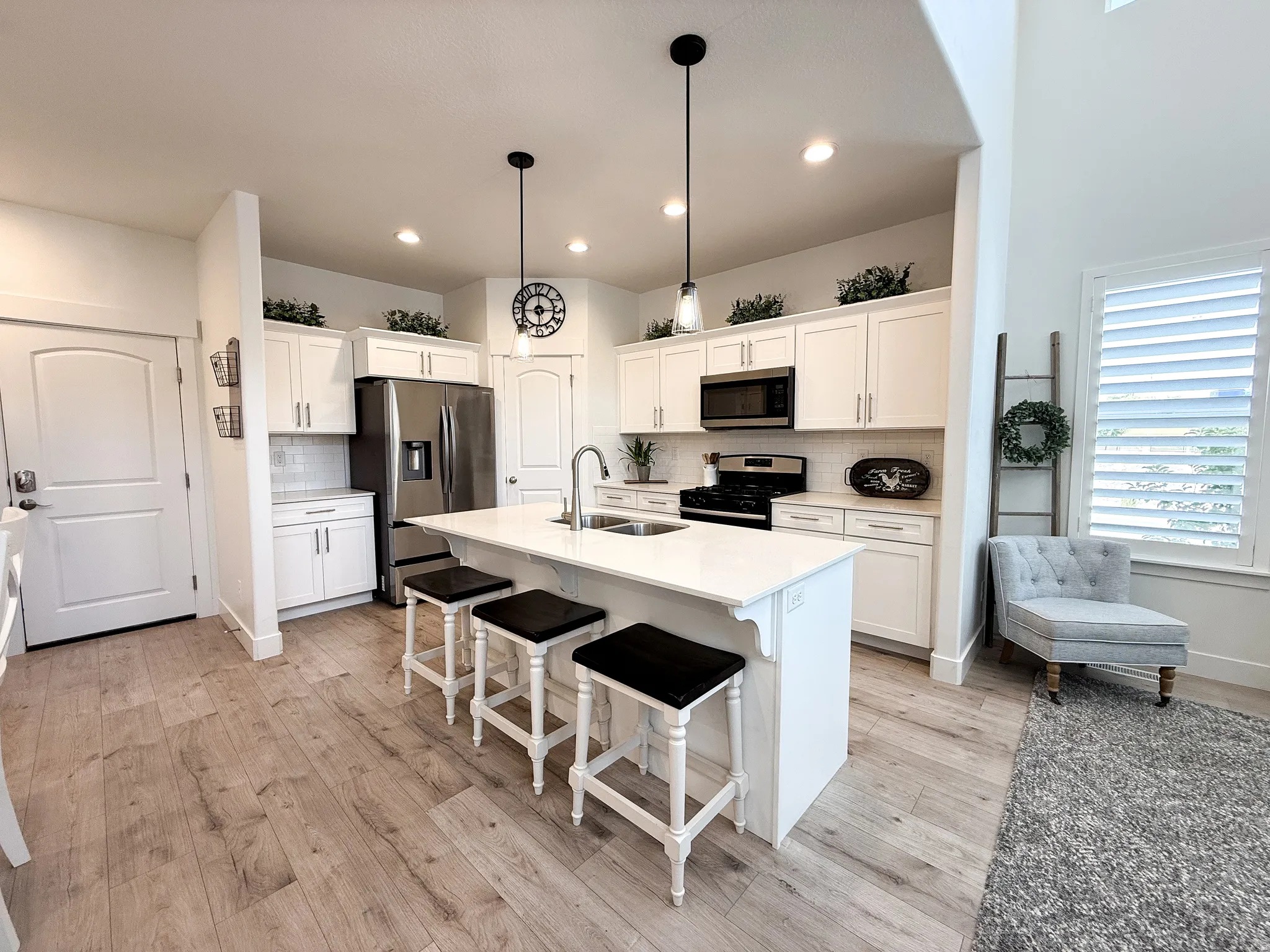 Open-concept kitchen featuring an oversized island with seating, white shaker cabinetry, stainless steel appliances, and wood-finish flooring