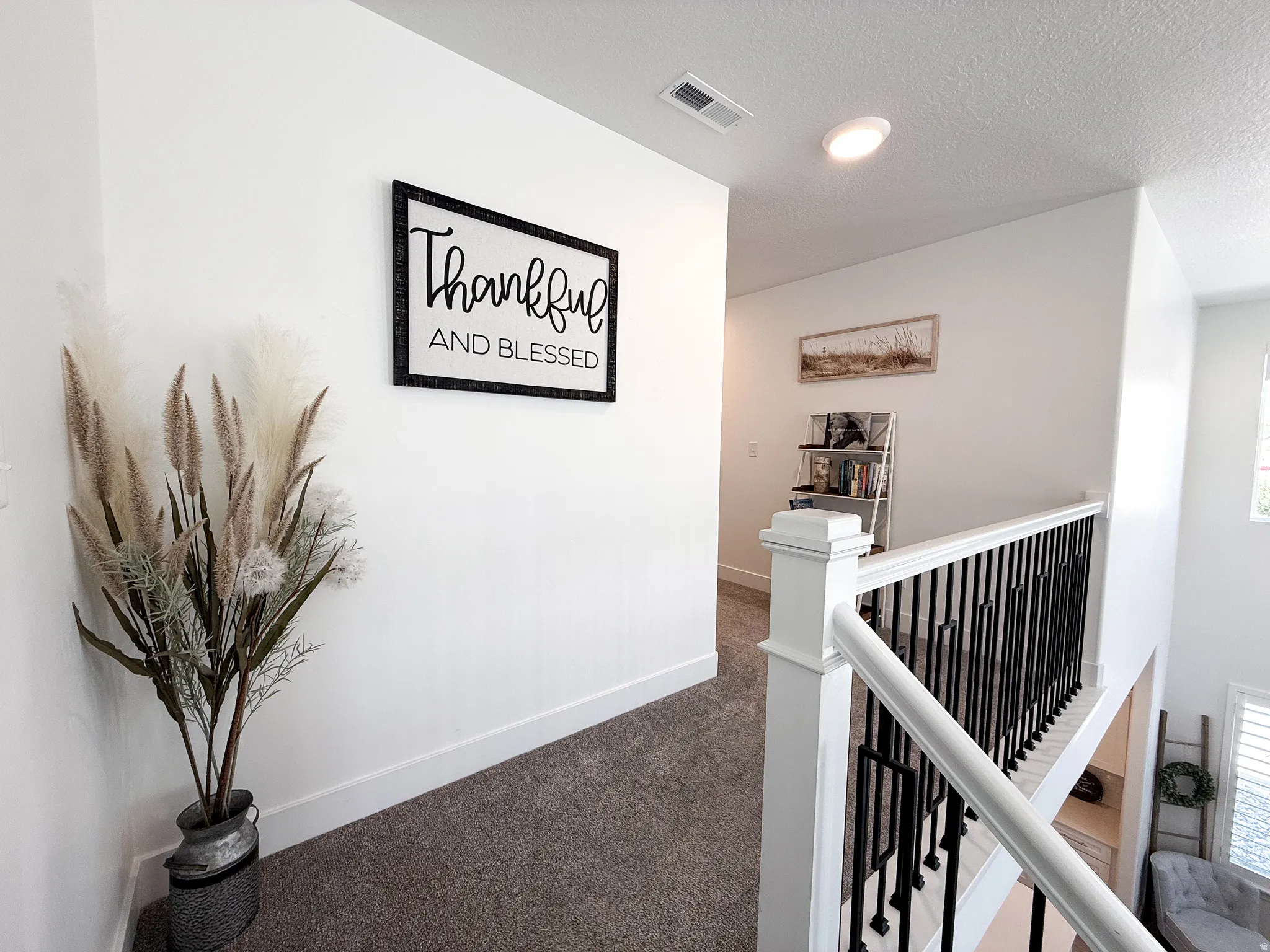 Upper landing featuring a white painted railing with black metal spindles and dark gray carpet flooring