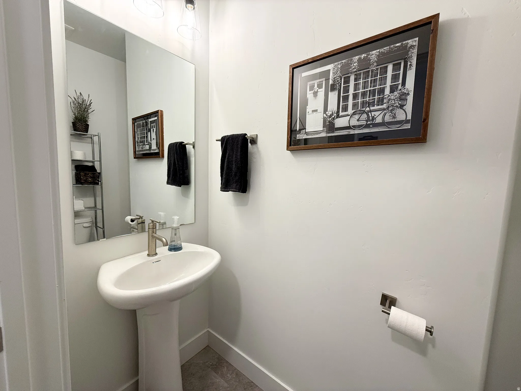 Modern pedestal sink with brushed nickel faucet, large wall-mounted mirror, and contemporary lighting fixture