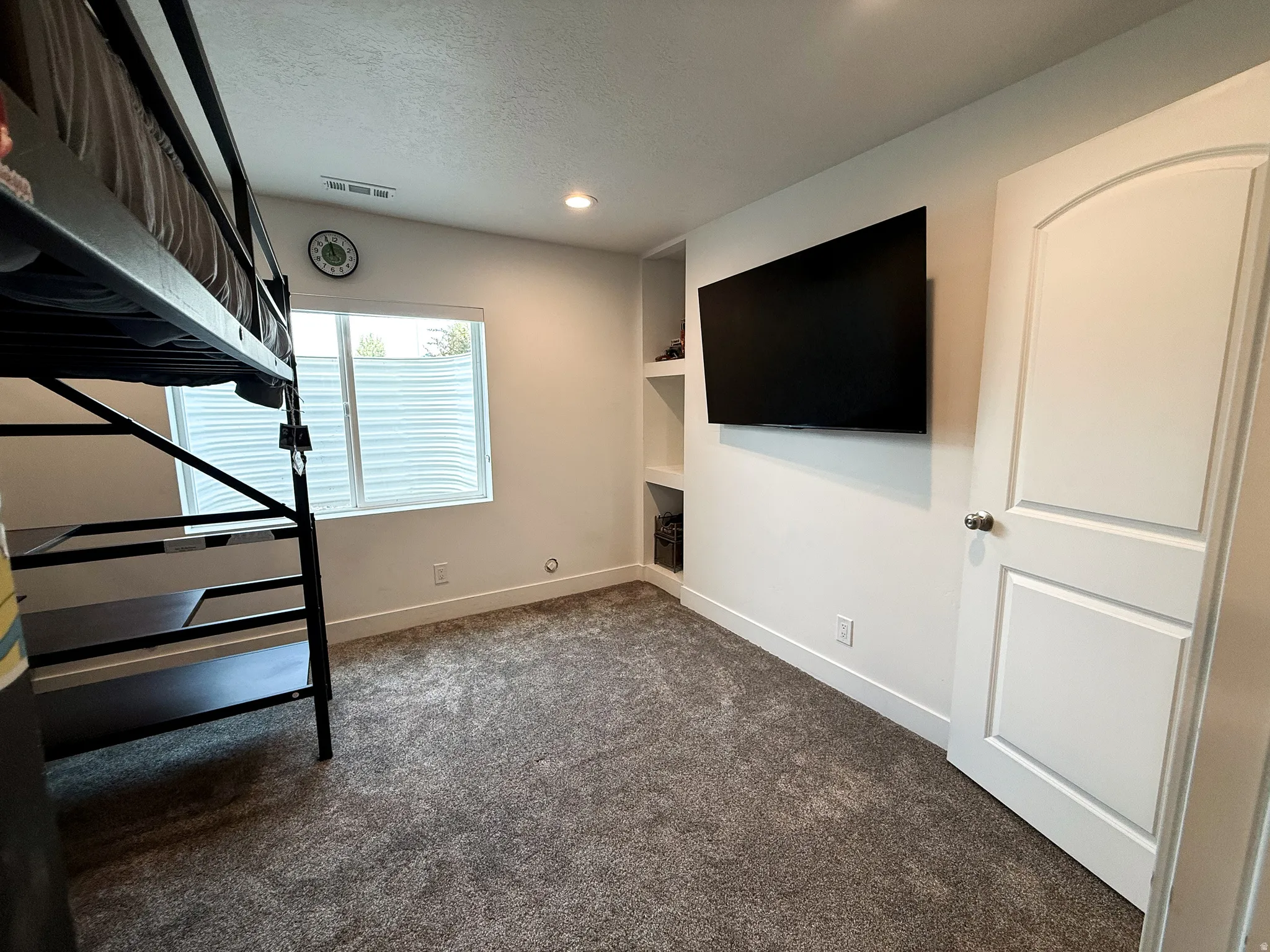 Room featuring neutral carpeting, a built-in wall unit with shelving, a recessed light, and a window with blinds