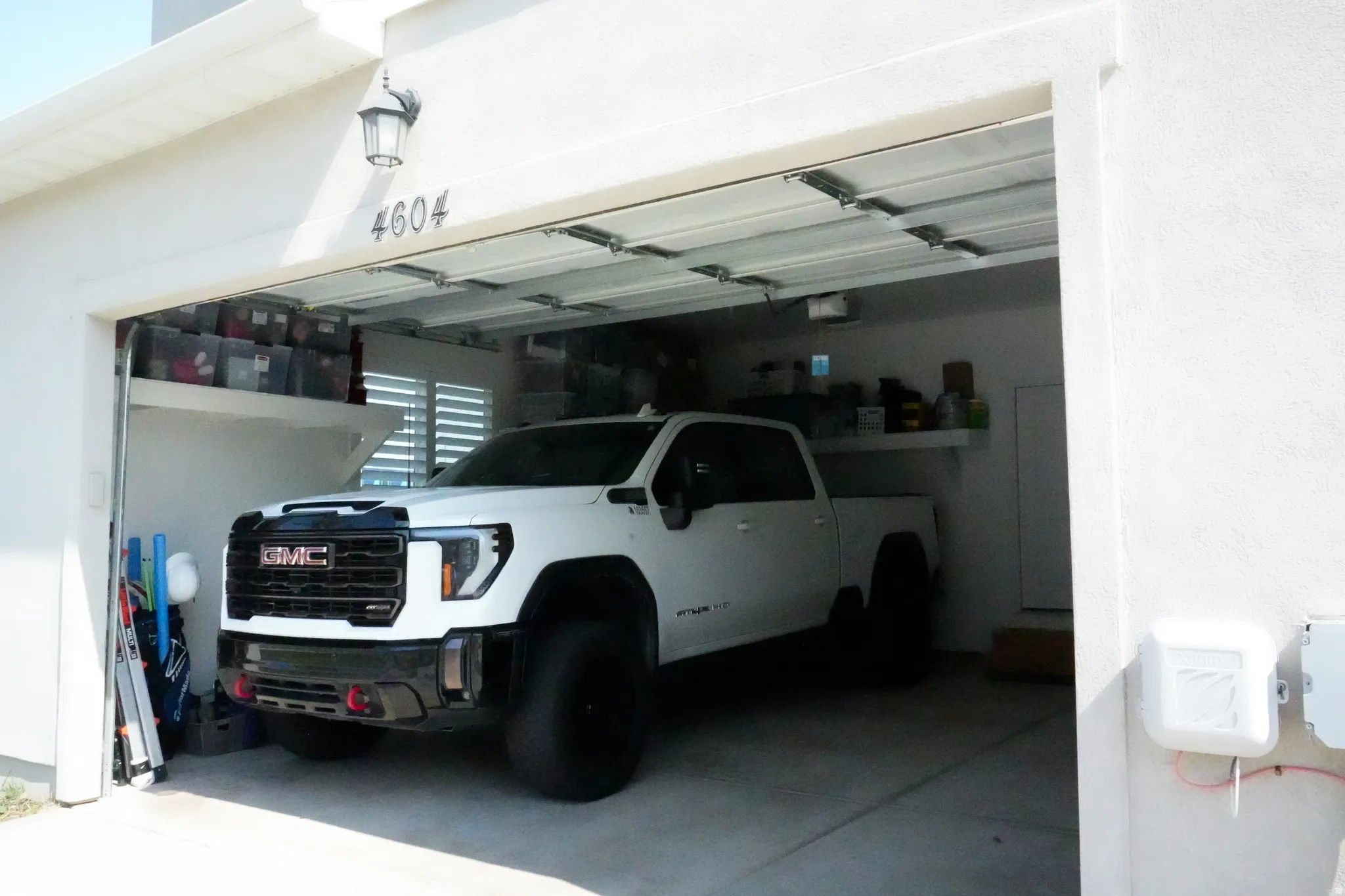 Attached two-car garage with white stucco exterior, integrated address numbers, and an overhead light fixture