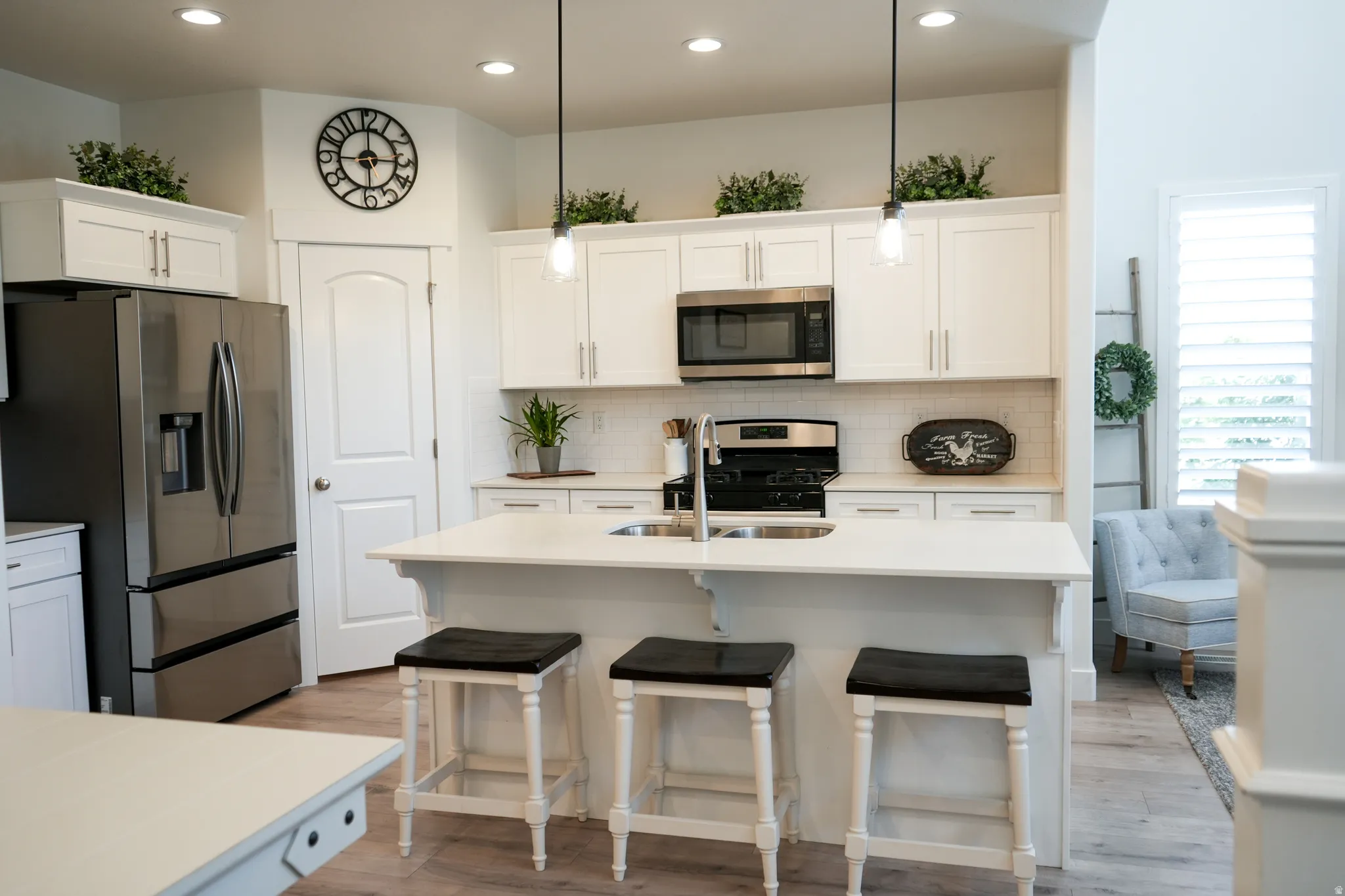 Kitchen featuring white cabinetry, stainless steel appliances, a center island with a built-in sink, pendant lighting, and wood-finish flooring