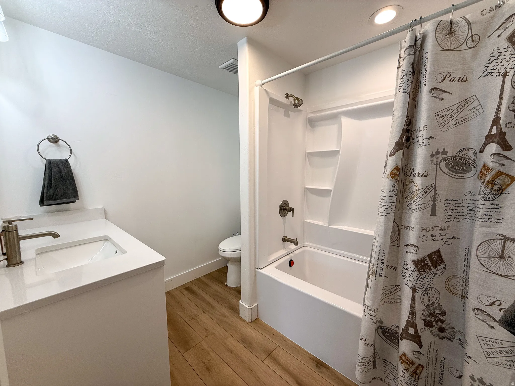 Bathroom featuring a white vanity with an integrated sink, brushed nickel faucet, wood-finish flooring, and a tub-shower combination with built-in shelving