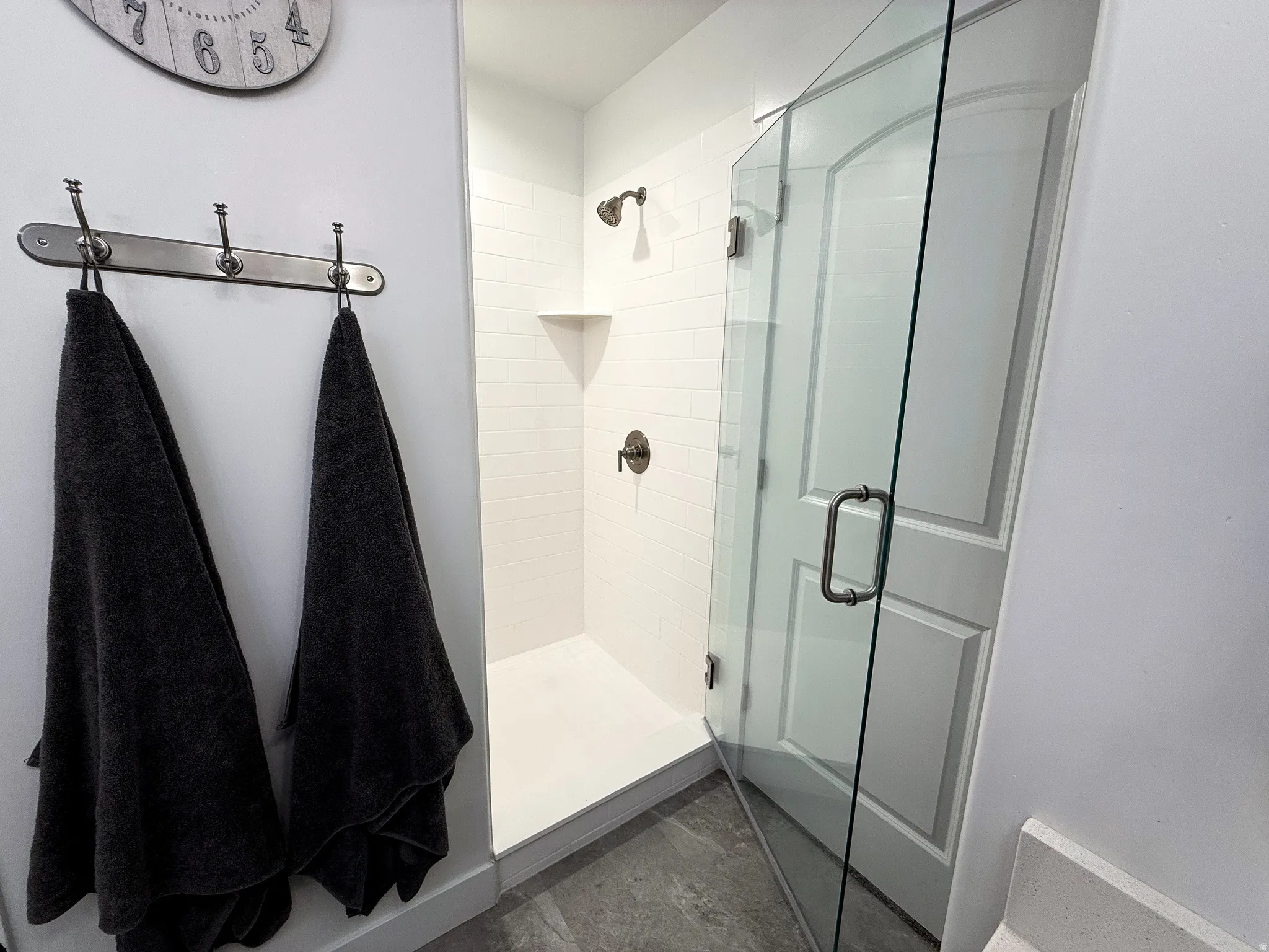 Walk-in shower featuring a frameless glass enclosure, white subway tile surround, integrated corner shelf, and dark bronze fixtures