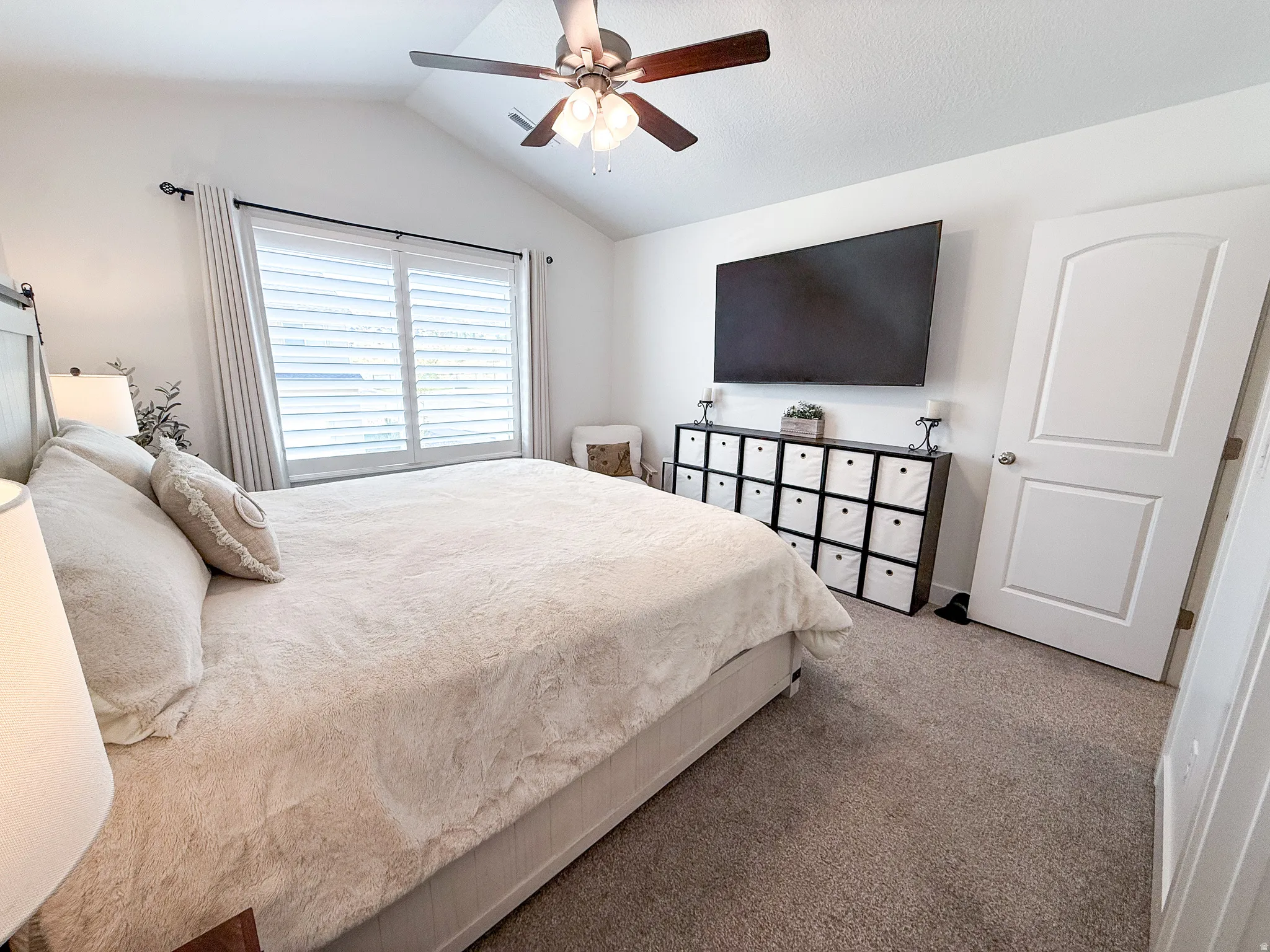 Spacious bedroom featuring vaulted ceilings, a ceiling fan with light fixture, plantation shutters, and soft carpet flooring