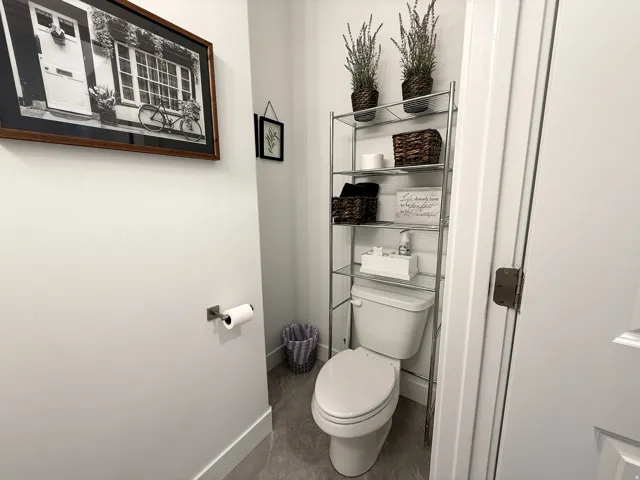 Compact water closet featuring a white commode, gray tile flooring, and white baseboards