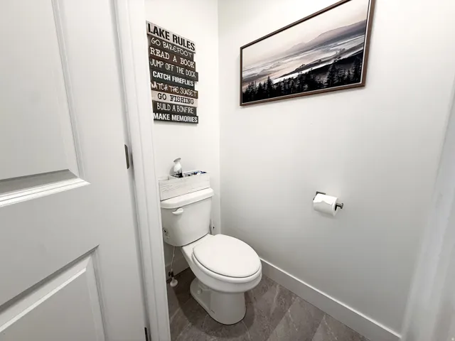 Compact powder room featuring a contemporary white toilet, grey tile flooring, and crisp white walls