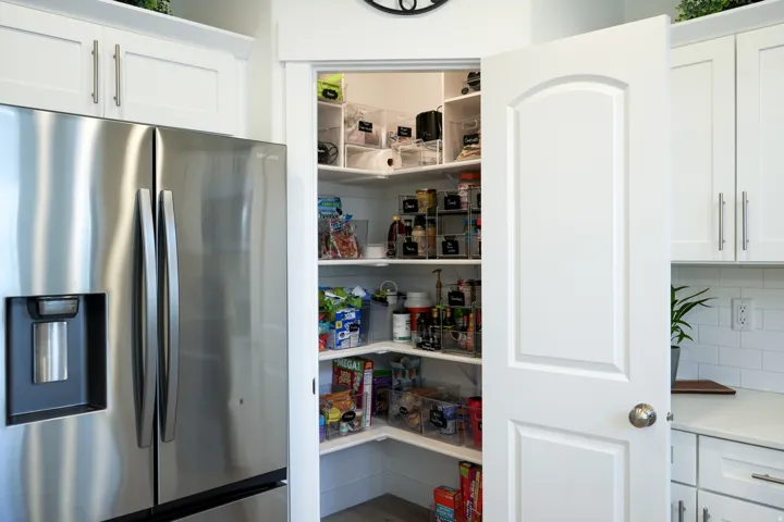 Walk-in pantry featuring white shelving, white paneled door, and wood-finish flooring