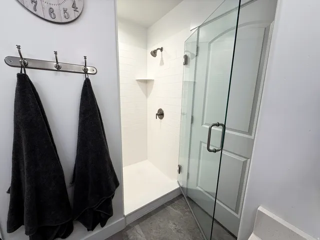 Walk-in shower featuring a frameless glass enclosure, white subway tile surround, integrated corner shelf, and dark bronze fixtures