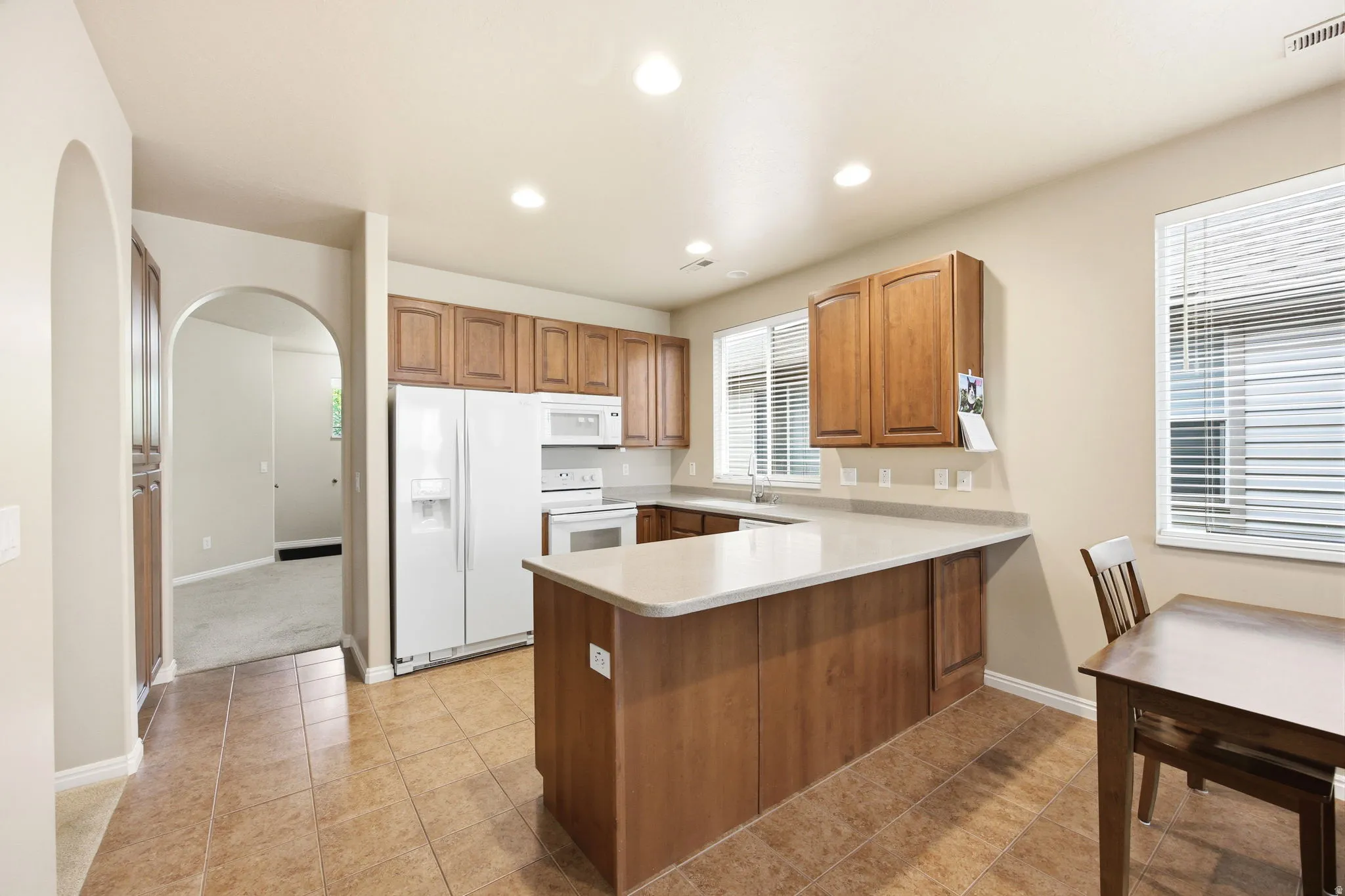 Kitchen featuring L-shaped light-toned countertops, wood cabinetry, white appliances, and recessed lighting